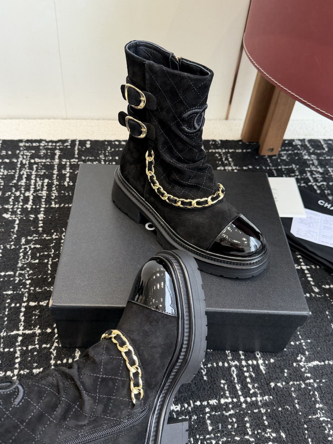 Pair of black Chanel quilted suede ankle boots with gold chain and patent leather toe caps on a black box - Hình 7