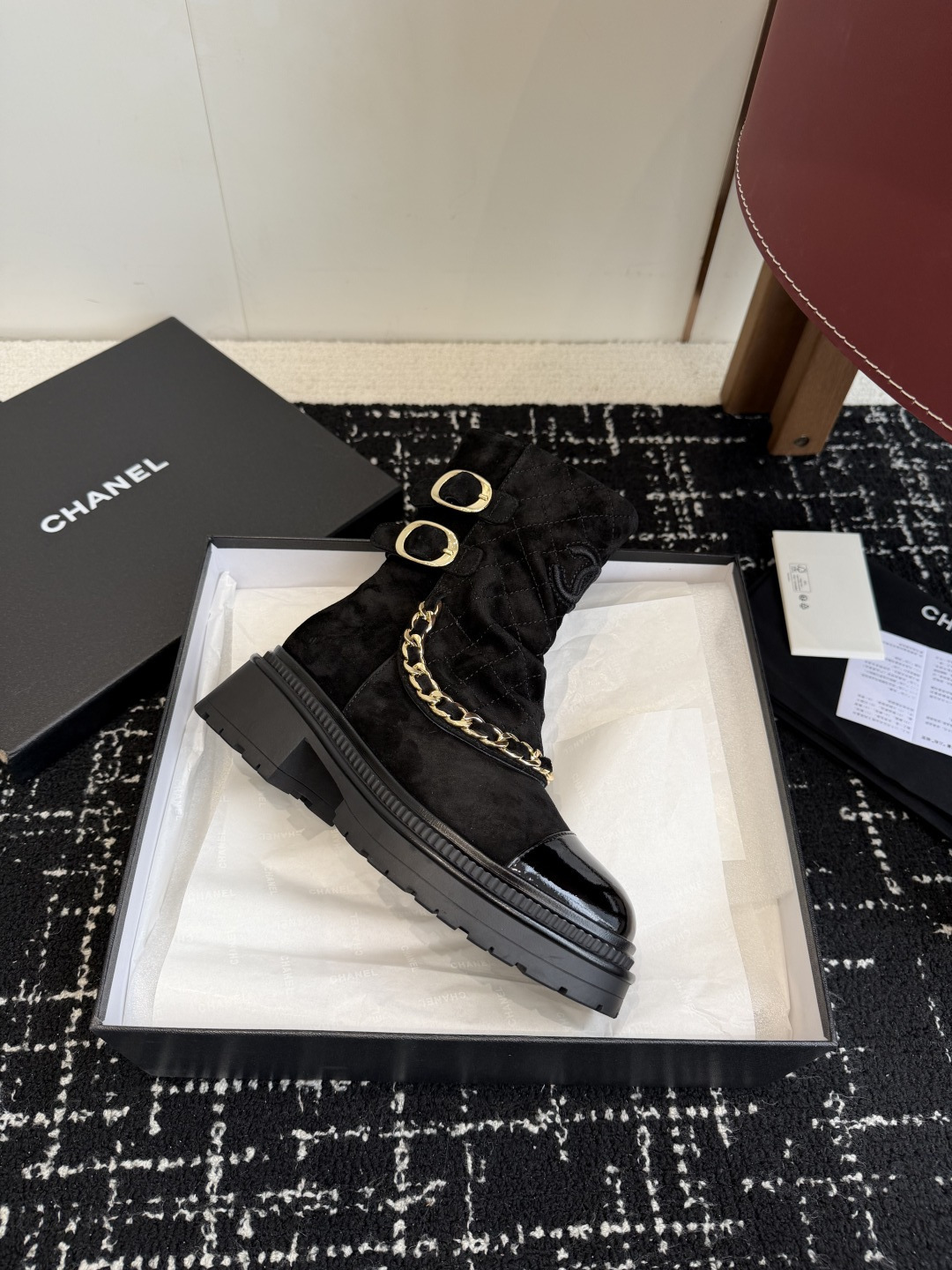 Pair of black Chanel quilted suede ankle boots with gold chain and patent leather toe caps on a black box - Hình 6