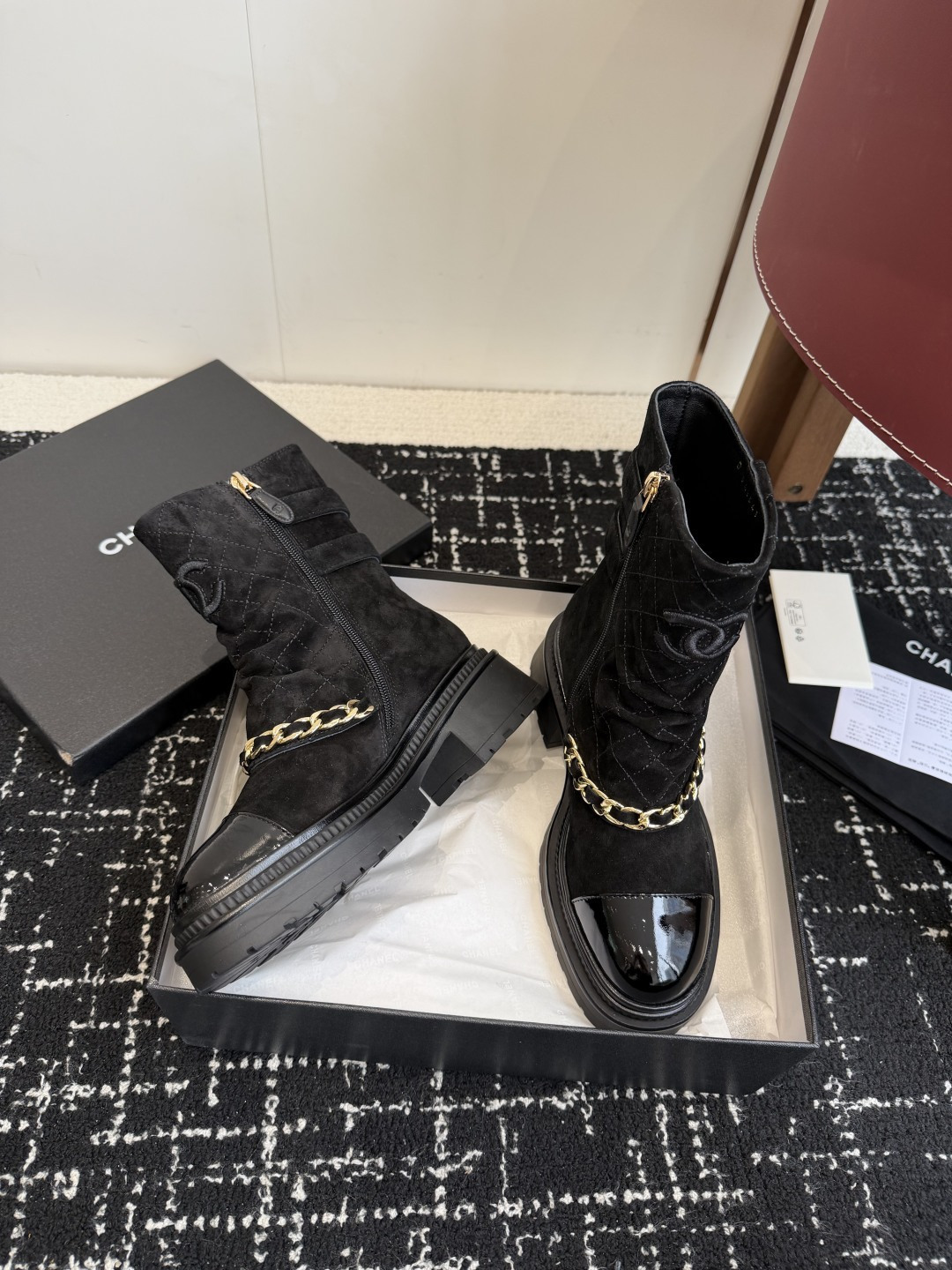 Pair of black Chanel quilted suede ankle boots with gold chain and patent leather toe caps on a black box - Hình 5