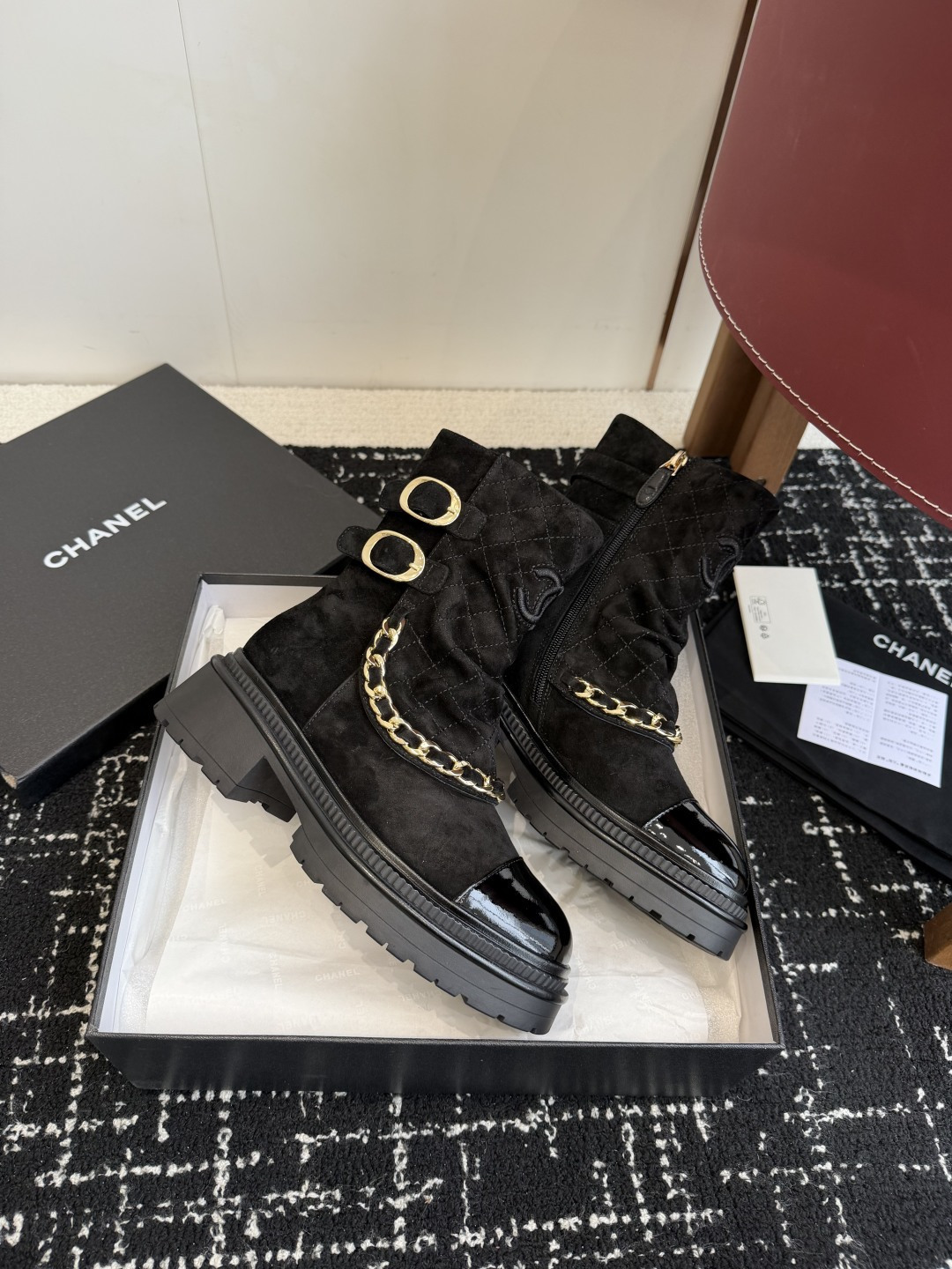 Pair of black Chanel quilted suede ankle boots with gold chain and patent leather toe caps on a black box - Hình 4