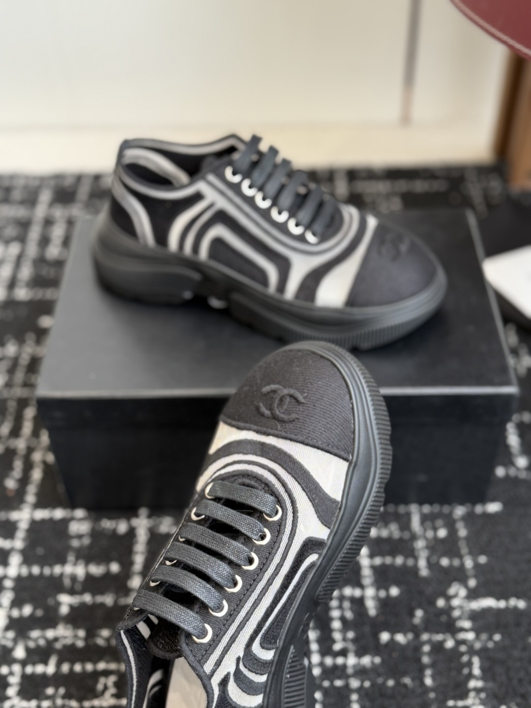 Pair of black and white Chanel mesh sneakers with wavy patterns and CC logo on a black box - Hình 5