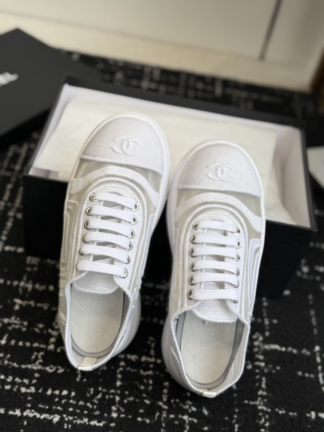 Pair of white Chanel sneakers with mesh panels and double C logo on the toe cap, placed on a black designer shoe box. - Hình 4