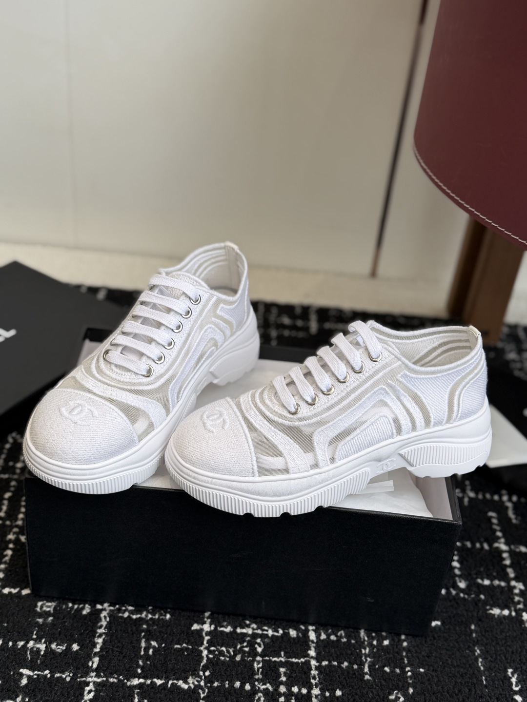 Pair of white Chanel sneakers with mesh panels and double C logo on the toe cap, placed on a black designer shoe box. - Hình 3