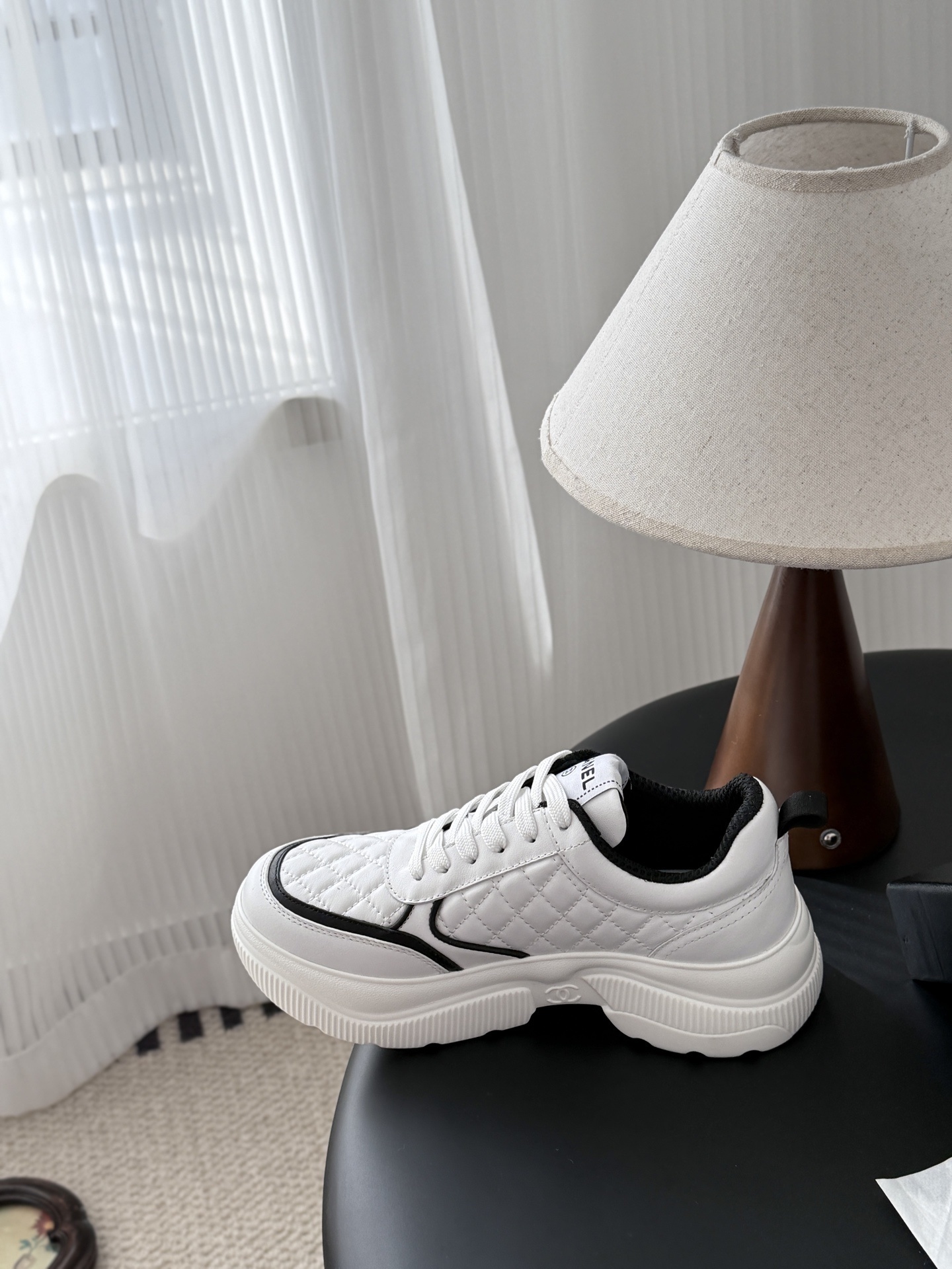 A pair of white Chanel quilted leather sneakers with black CC logo and chunky white soles next to a black Chanel box - Hình 8