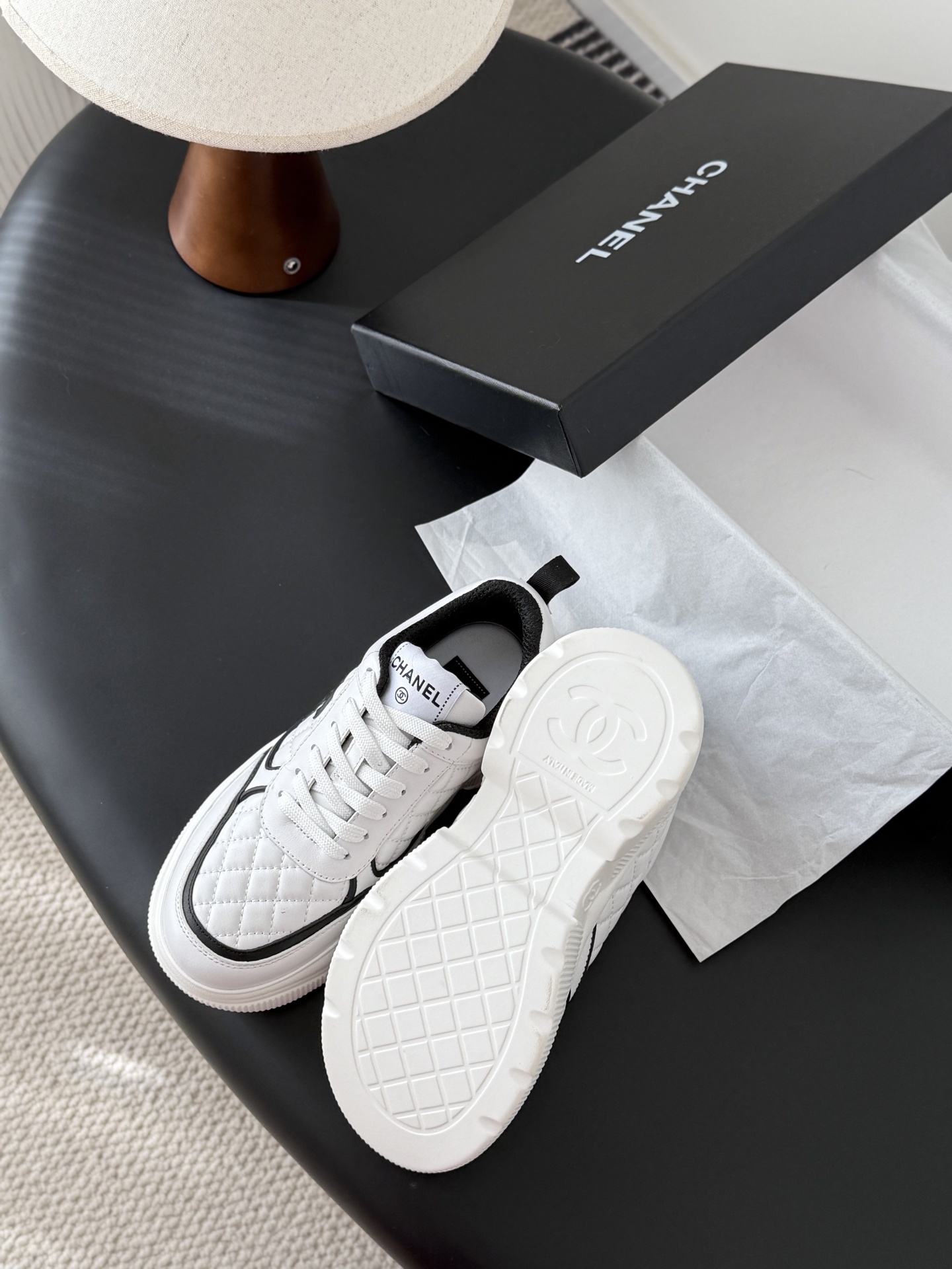 A pair of white Chanel quilted leather sneakers with black CC logo and chunky white soles next to a black Chanel box - Hình 5