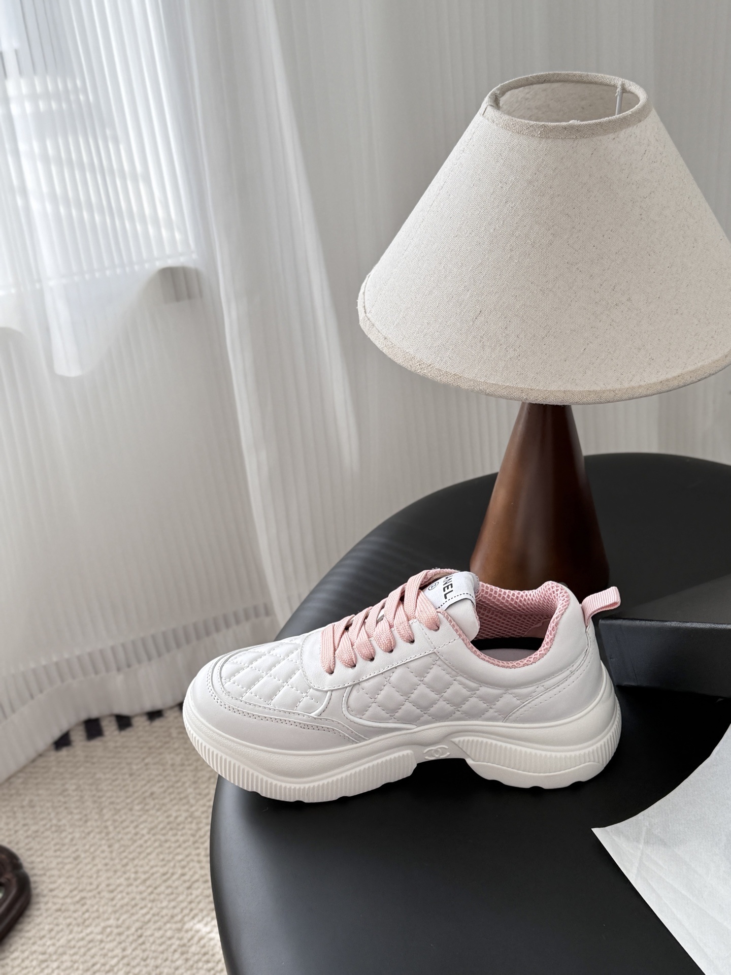 A pair of Chanel white quilted sneakers with pink laces and pink interior lining next to a black Chanel shoe box - Hình 8