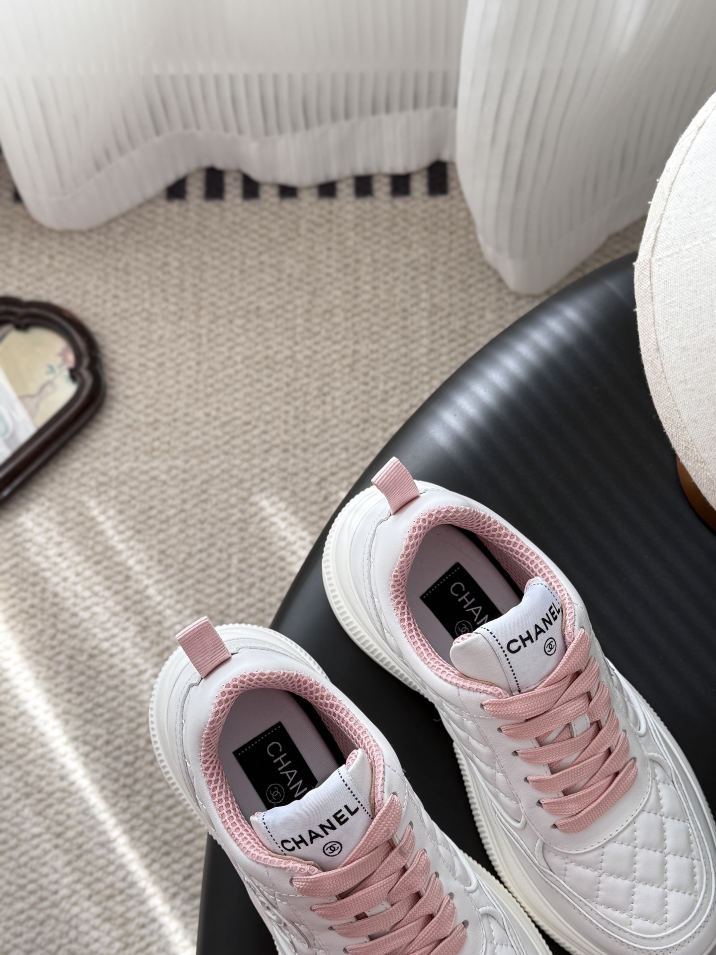 A pair of Chanel white quilted sneakers with pink laces and pink interior lining next to a black Chanel shoe box - Hình 7