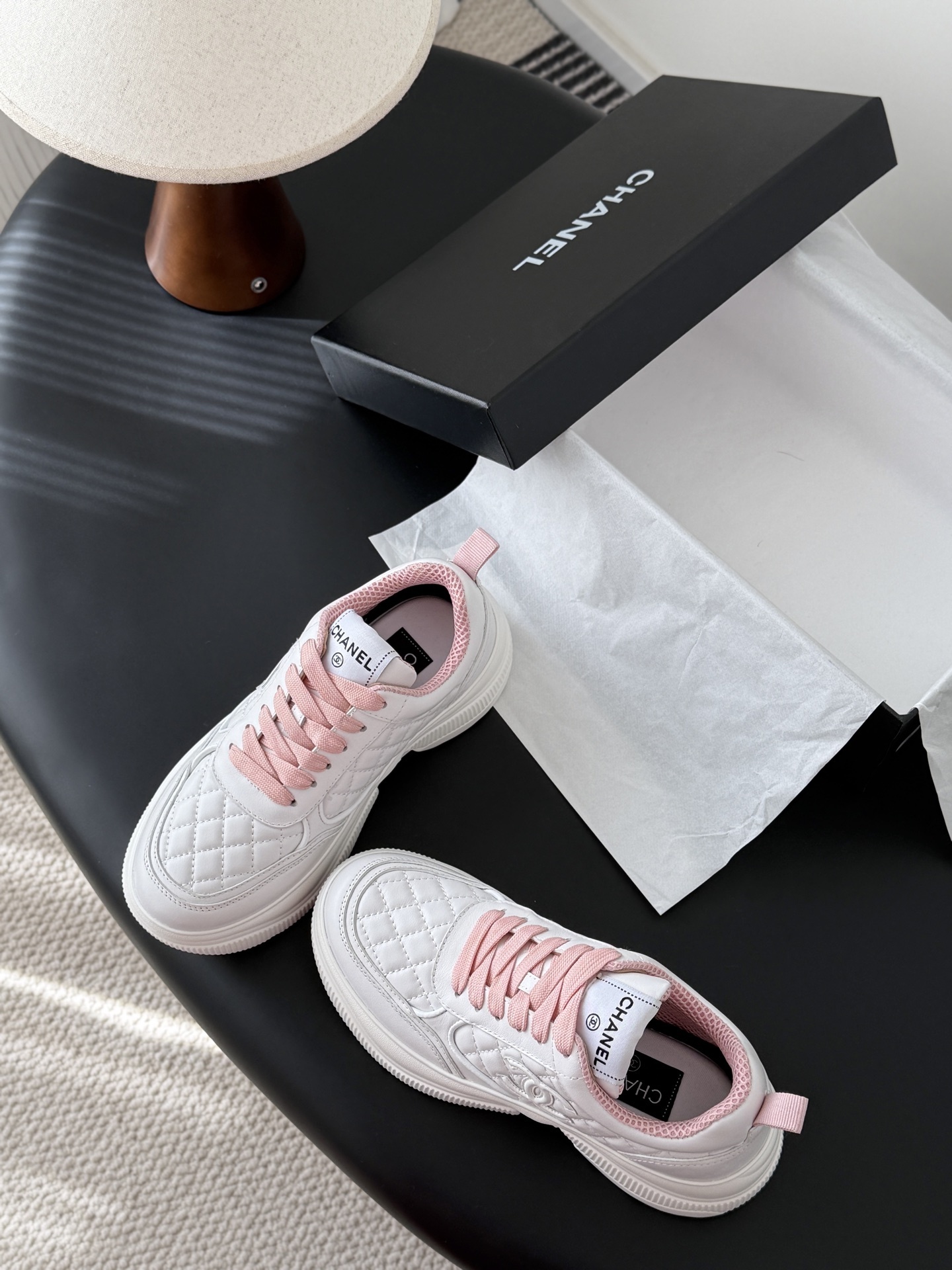 A pair of Chanel white quilted sneakers with pink laces and pink interior lining next to a black Chanel shoe box - Hình 6