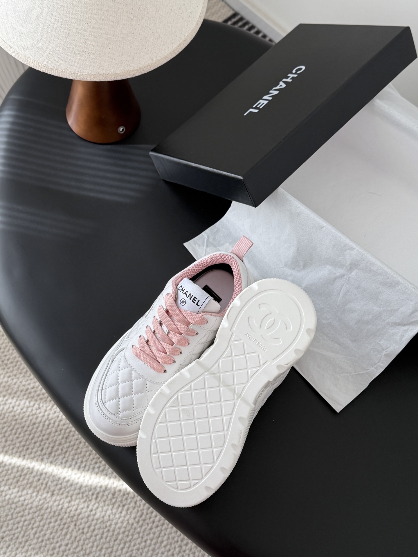 A pair of Chanel white quilted sneakers with pink laces and pink interior lining next to a black Chanel shoe box - Hình 5