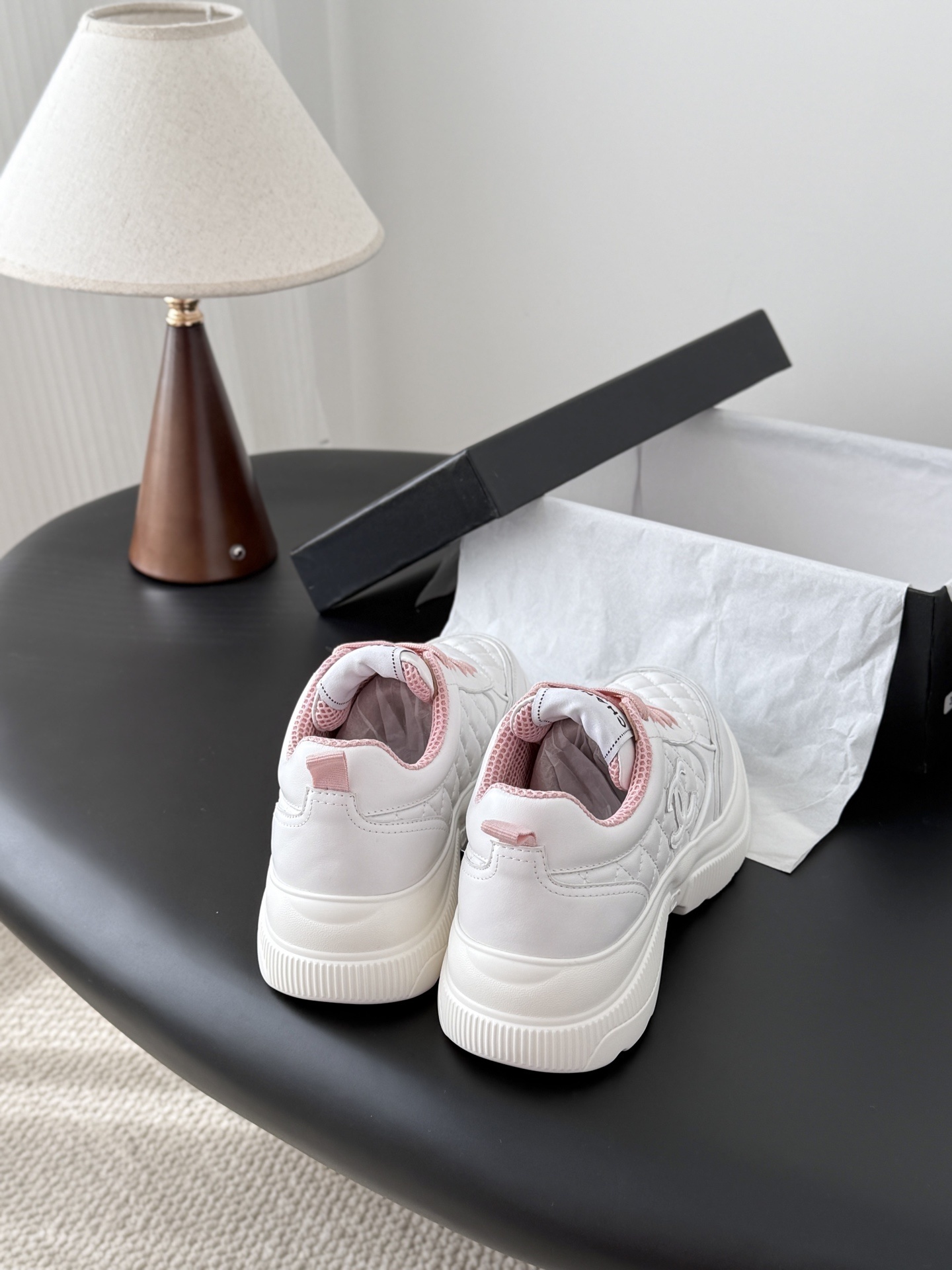 A pair of Chanel white quilted sneakers with pink laces and pink interior lining next to a black Chanel shoe box - Hình 3