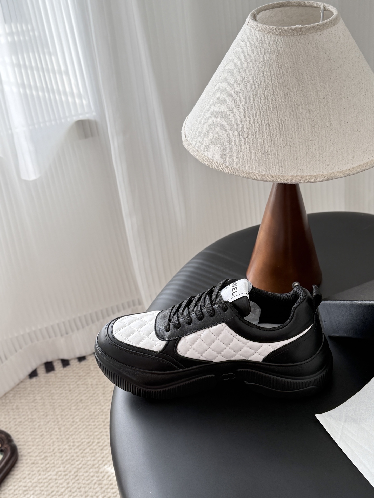 Pair of black and white Chanel quilted leather sneakers with CC logo on a black table next to a branded box - Hình 8