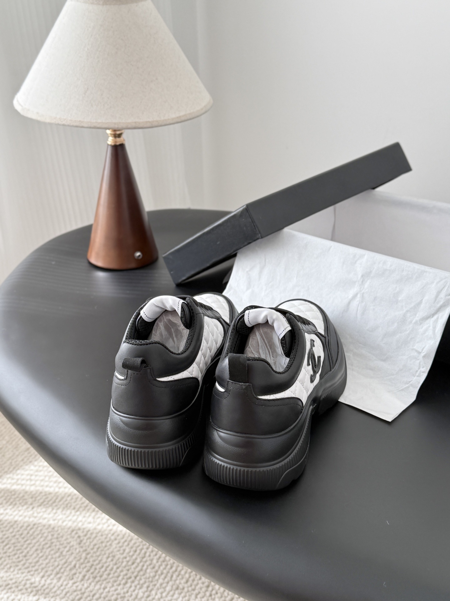 Pair of black and white Chanel quilted leather sneakers with CC logo on a black table next to a branded box - Hình 3