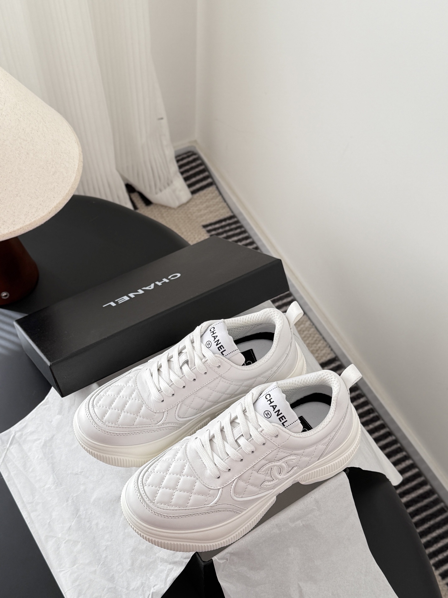 A pair of luxury Chanel white quilted leather sneakers next to their original black designer box - Hình 9