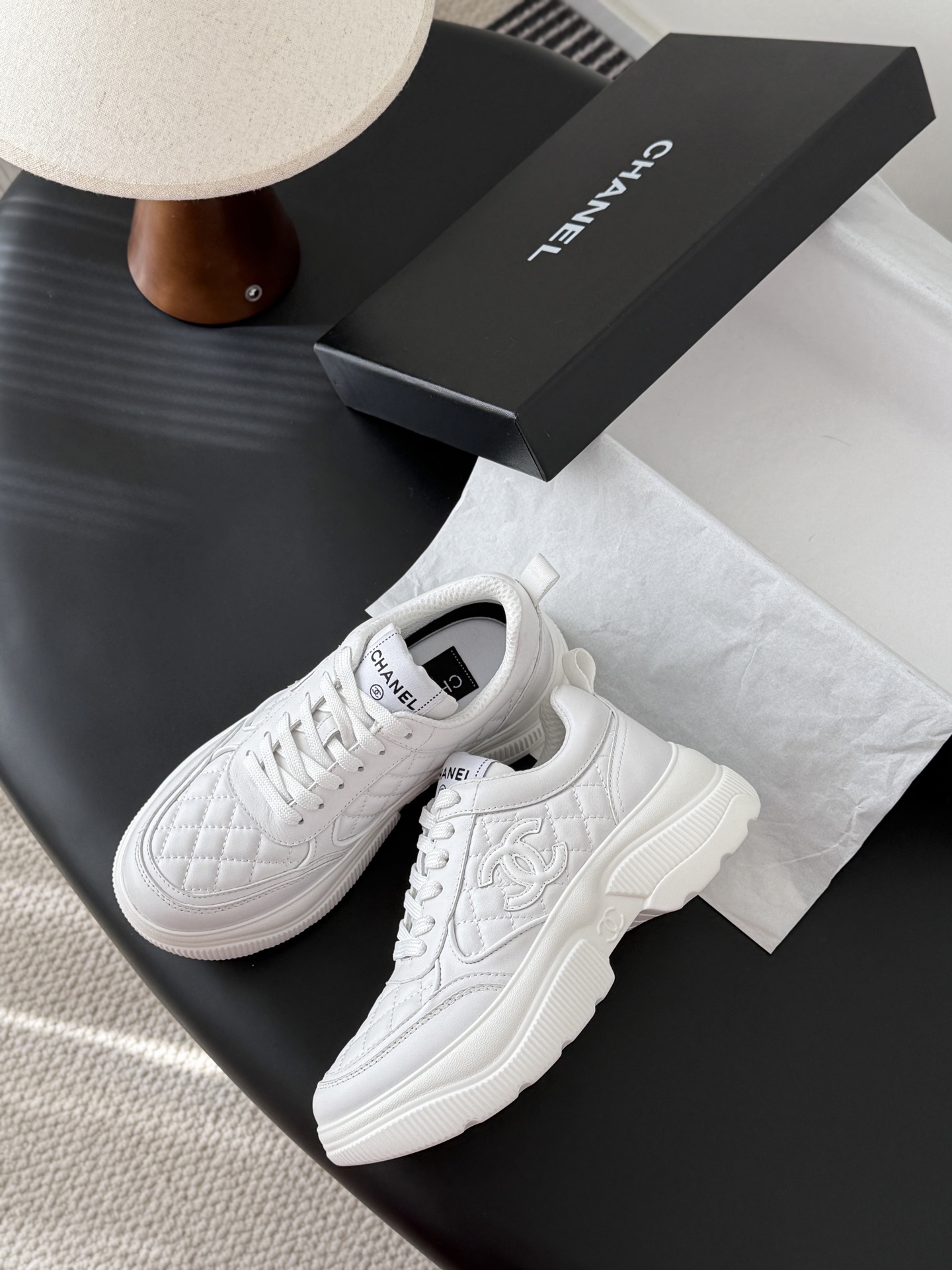A pair of luxury Chanel white quilted leather sneakers next to their original black designer box - Hình 4