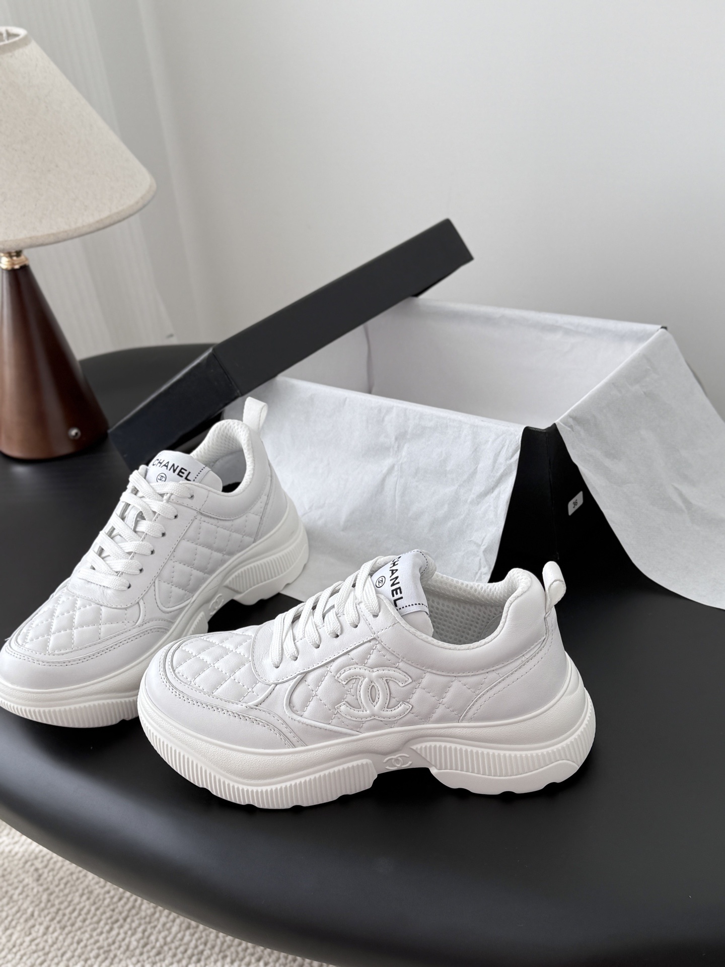 A pair of luxury Chanel white quilted leather sneakers next to their original black designer box - Hình 2