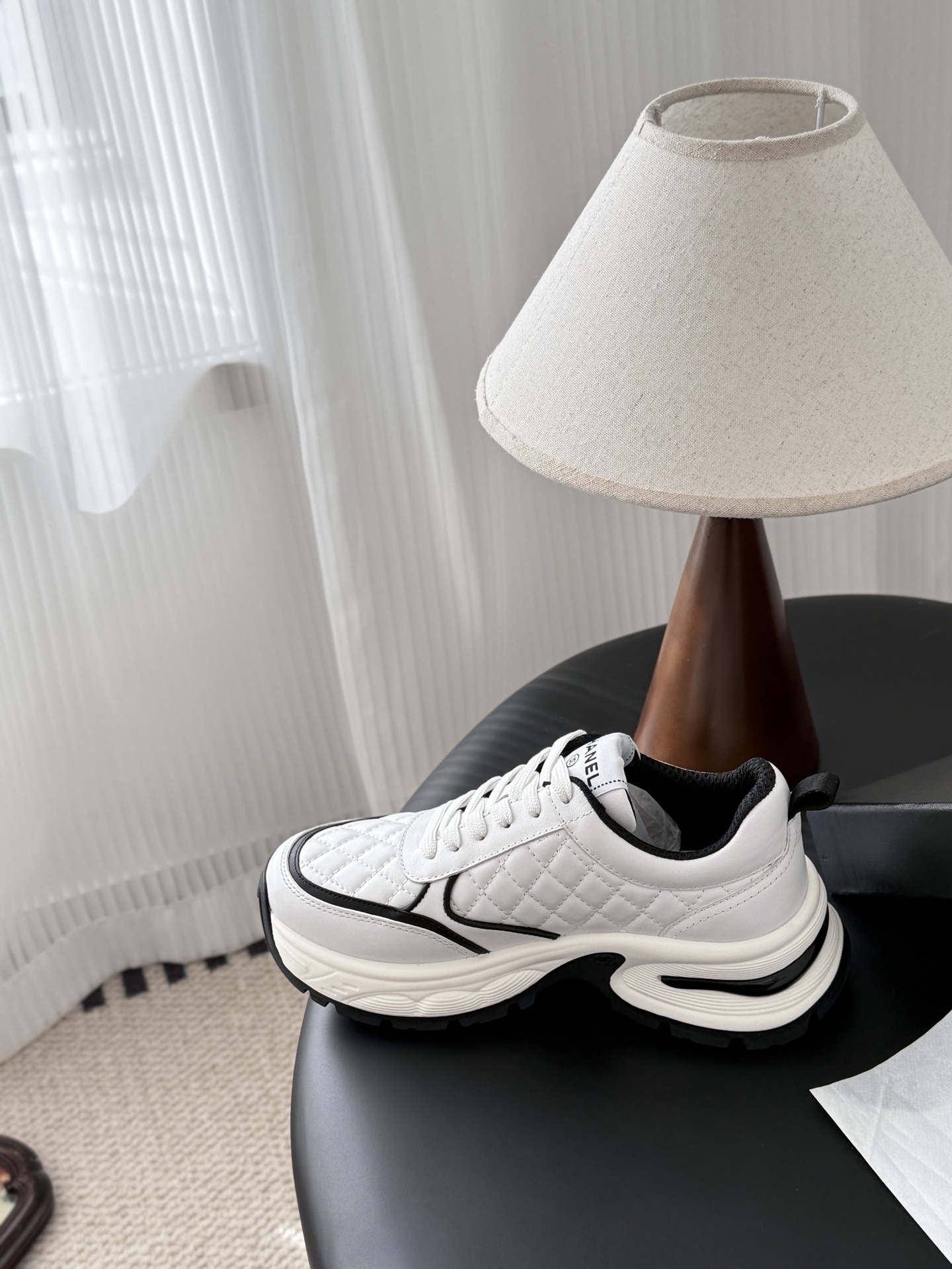 A pair of white Chanel chunky sneakers with black quilted details and CC logo displayed on a table next to a black Chanel box. - Hình 8