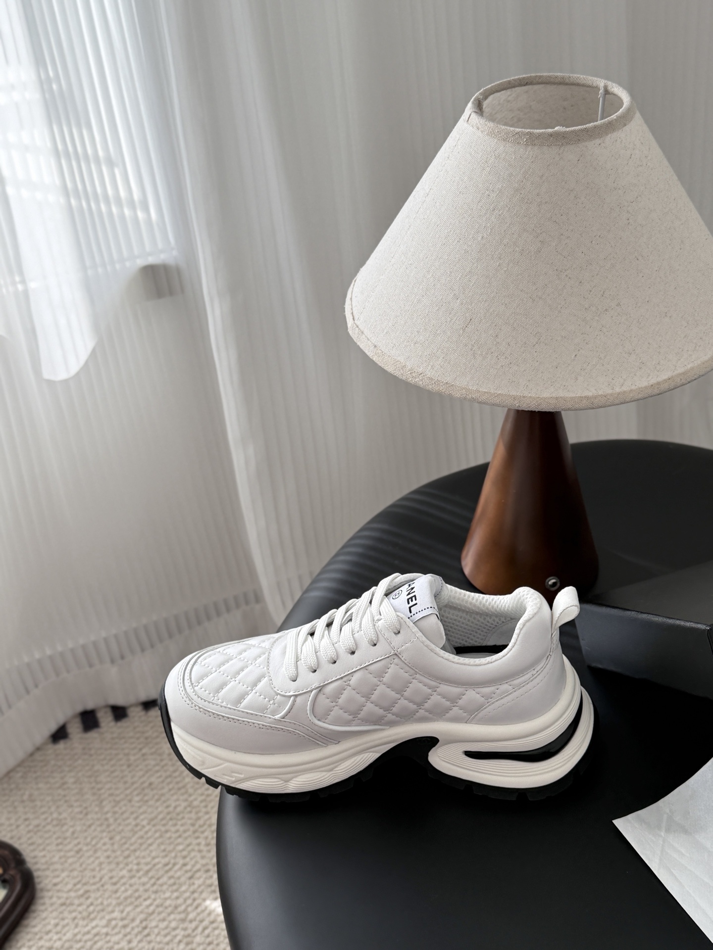 A pair of luxury white Chanel quilted leather sneakers with chunky soles and CC logo on a black table - Hình 8