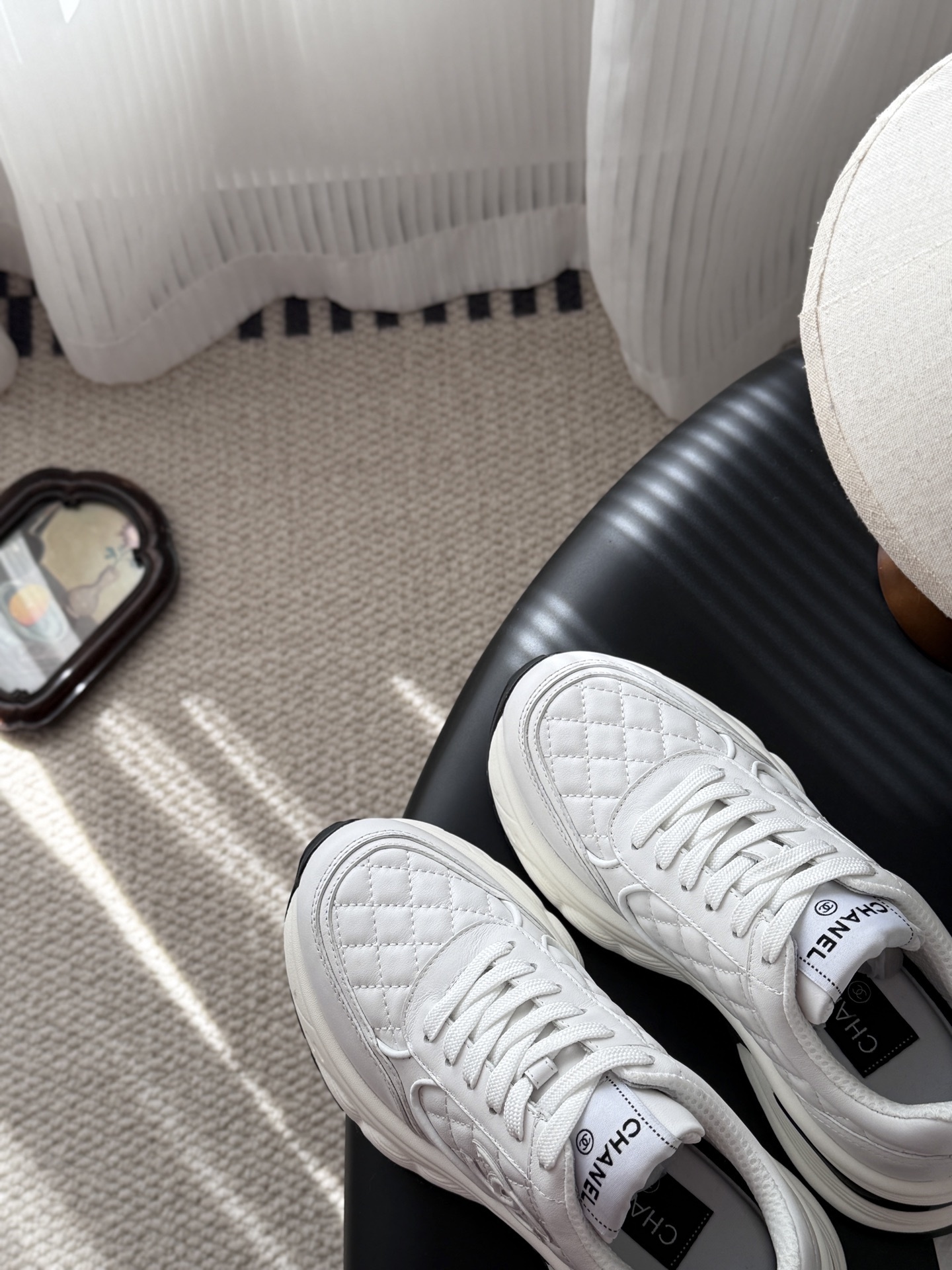 A pair of luxury white Chanel quilted leather sneakers with chunky soles and CC logo on a black table - Hình 7