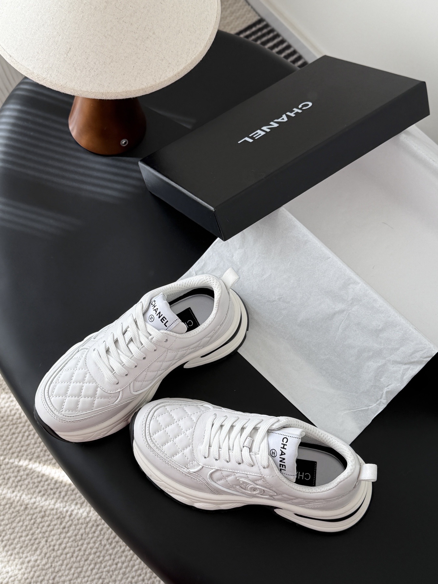 A pair of luxury white Chanel quilted leather sneakers with chunky soles and CC logo on a black table - Hình 6