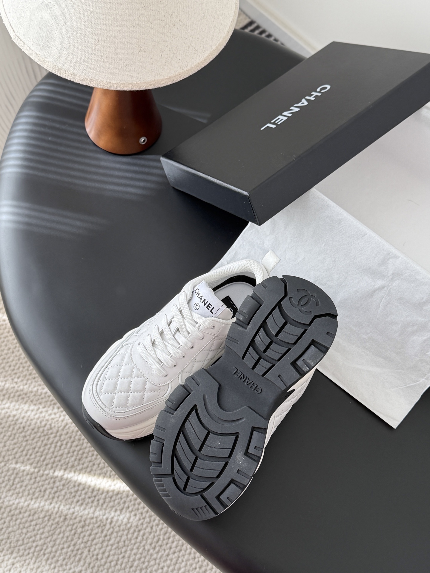 A pair of luxury white Chanel quilted leather sneakers with chunky soles and CC logo on a black table - Hình 5