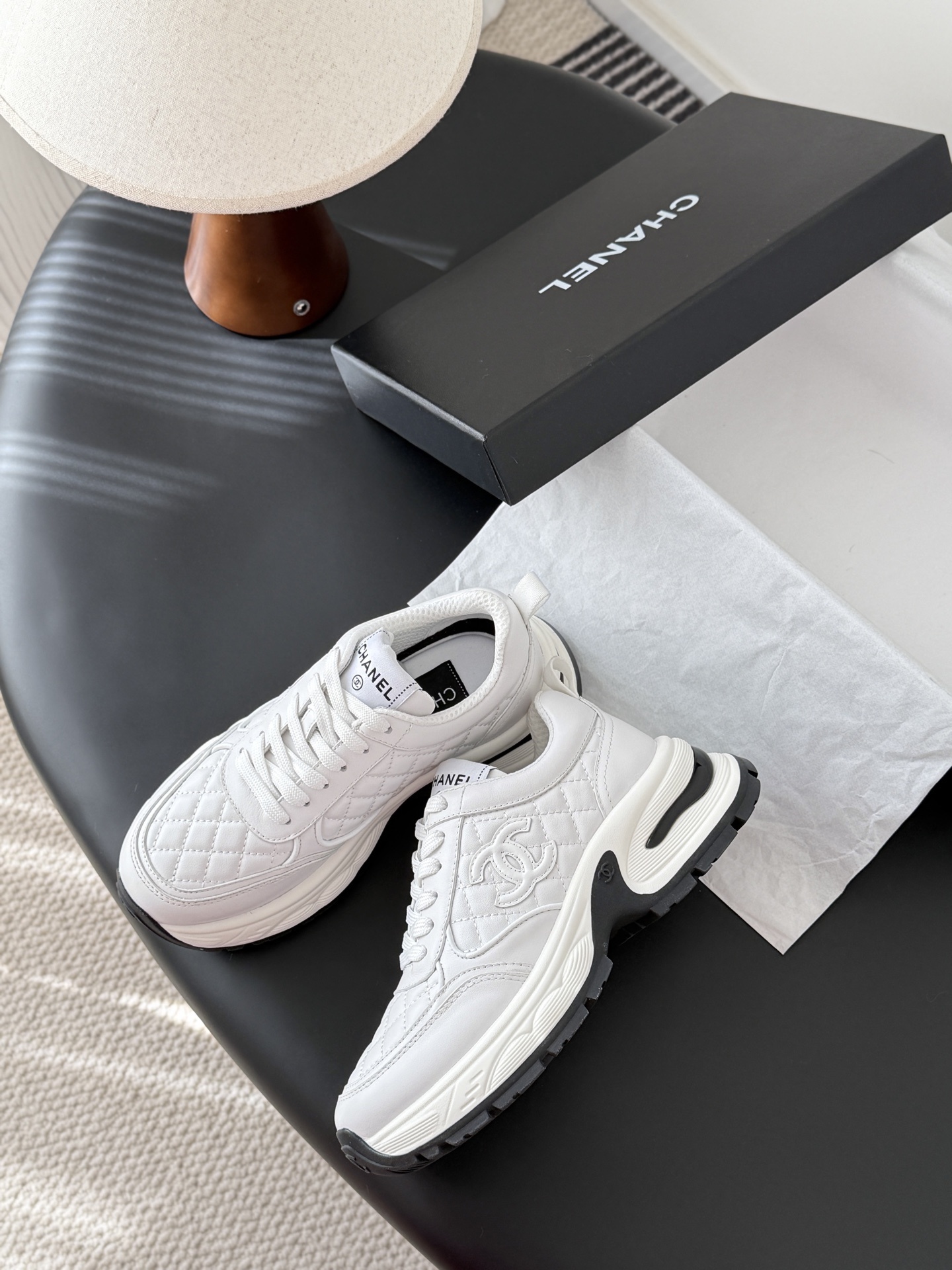 A pair of luxury white Chanel quilted leather sneakers with chunky soles and CC logo on a black table - Hình 4