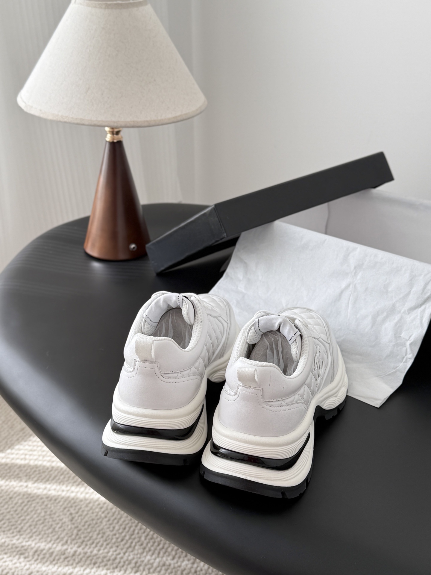A pair of luxury white Chanel quilted leather sneakers with chunky soles and CC logo on a black table - Hình 3