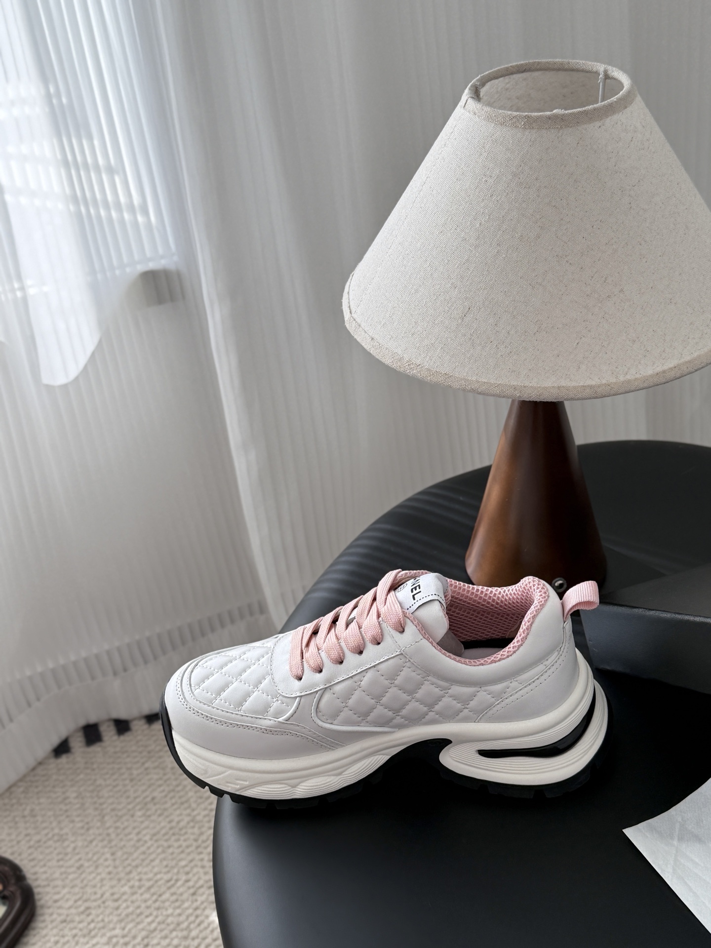 A pair of luxury white Chanel sneakers with pink laces and quilted leather detailing displayed next to a black Chanel shoe box. - Hình 8