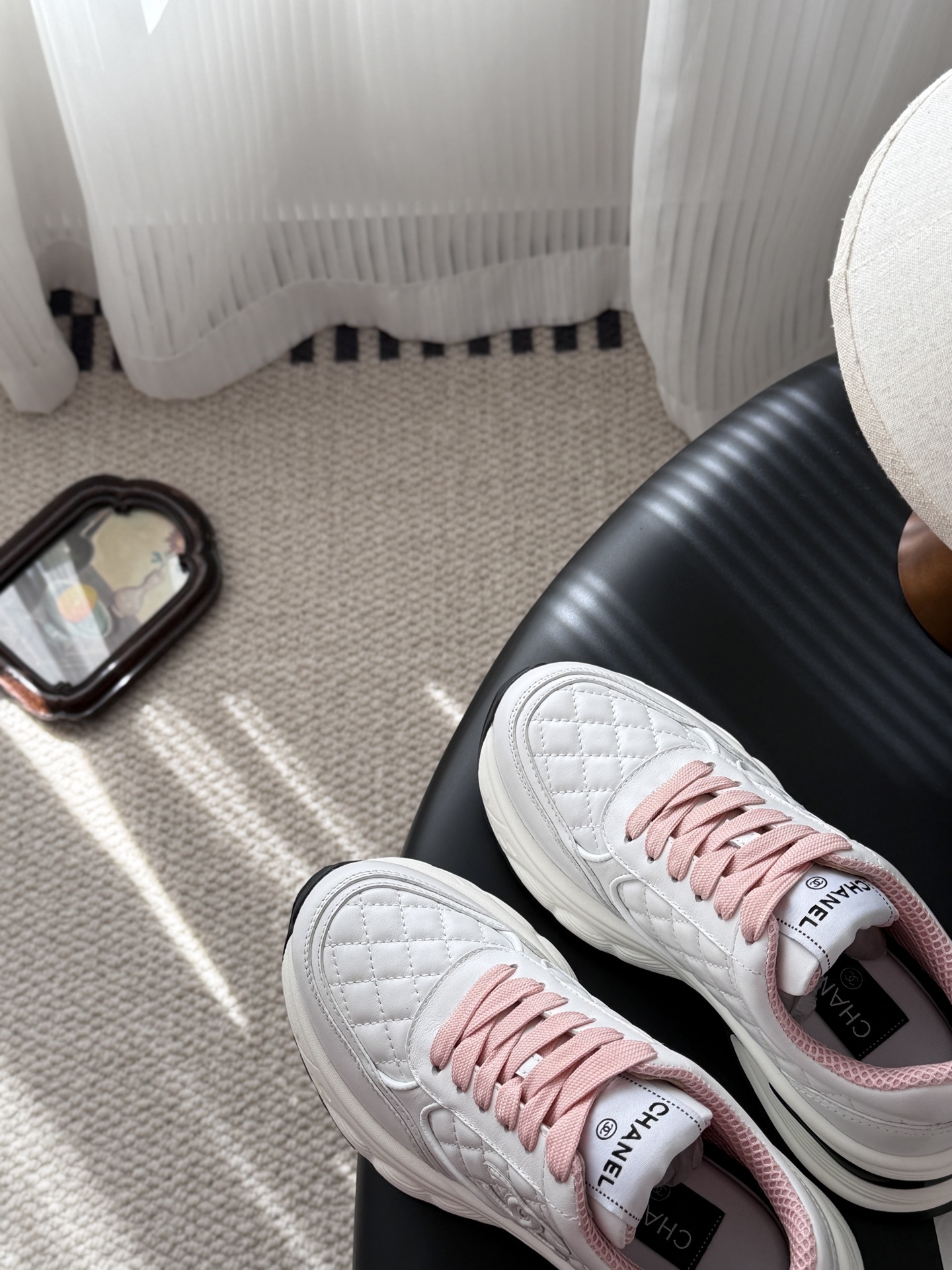 A pair of luxury white Chanel sneakers with pink laces and quilted leather detailing displayed next to a black Chanel shoe box. - Hình 7