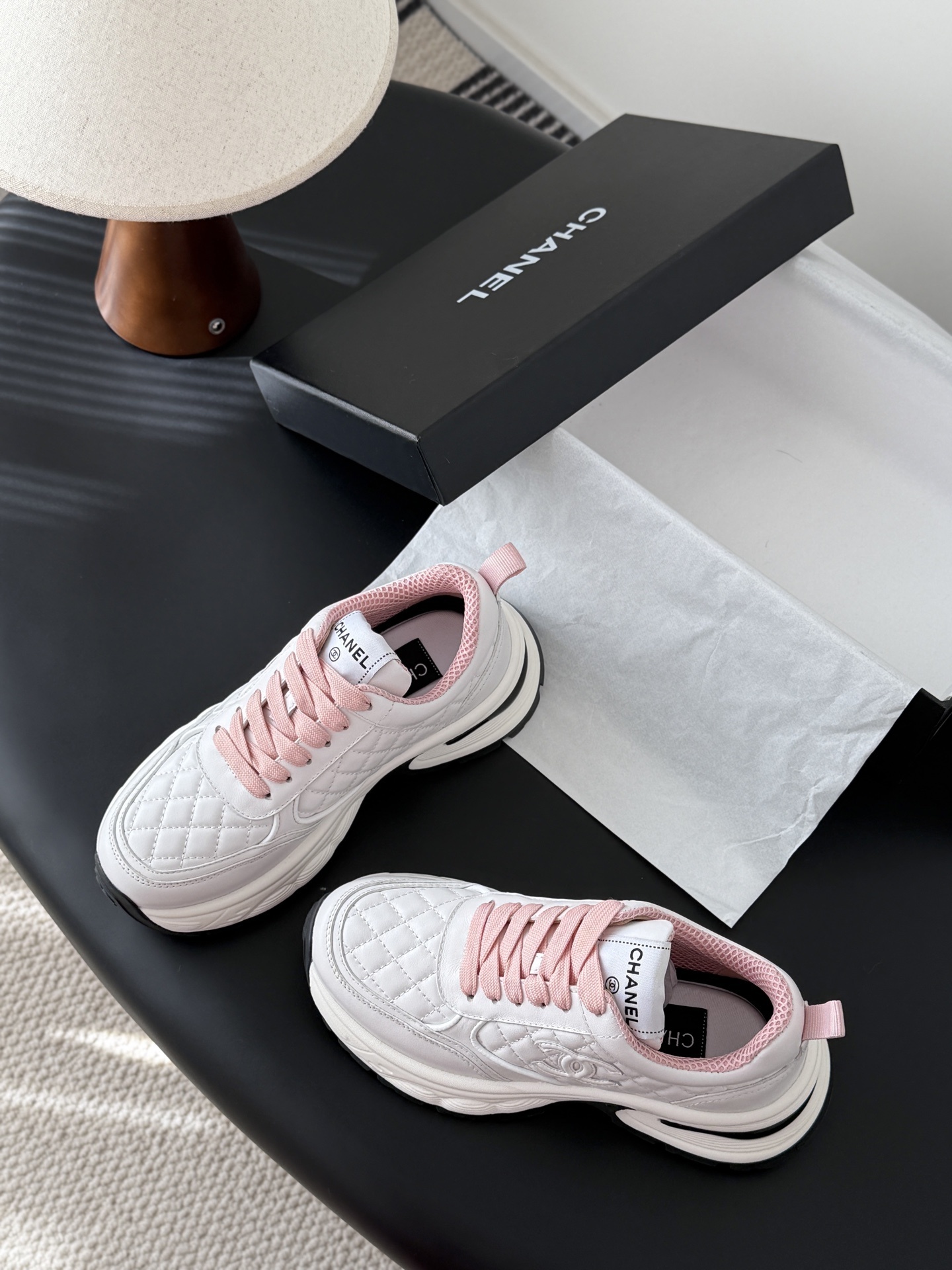 A pair of luxury white Chanel sneakers with pink laces and quilted leather detailing displayed next to a black Chanel shoe box. - Hình 6