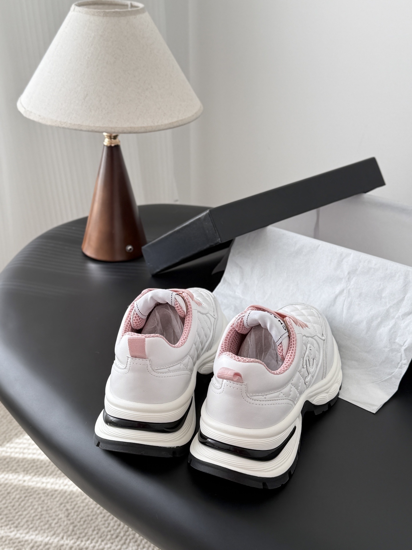A pair of luxury white Chanel sneakers with pink laces and quilted leather detailing displayed next to a black Chanel shoe box. - Hình 3