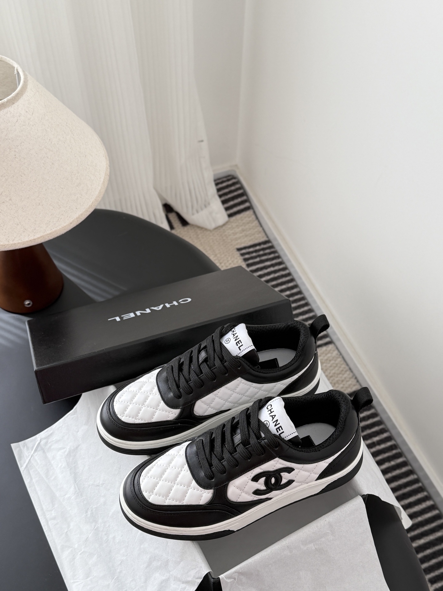 A pair of luxury Chanel black and white quilted leather sneakers with CC logo next to their original black box. - Hình 9