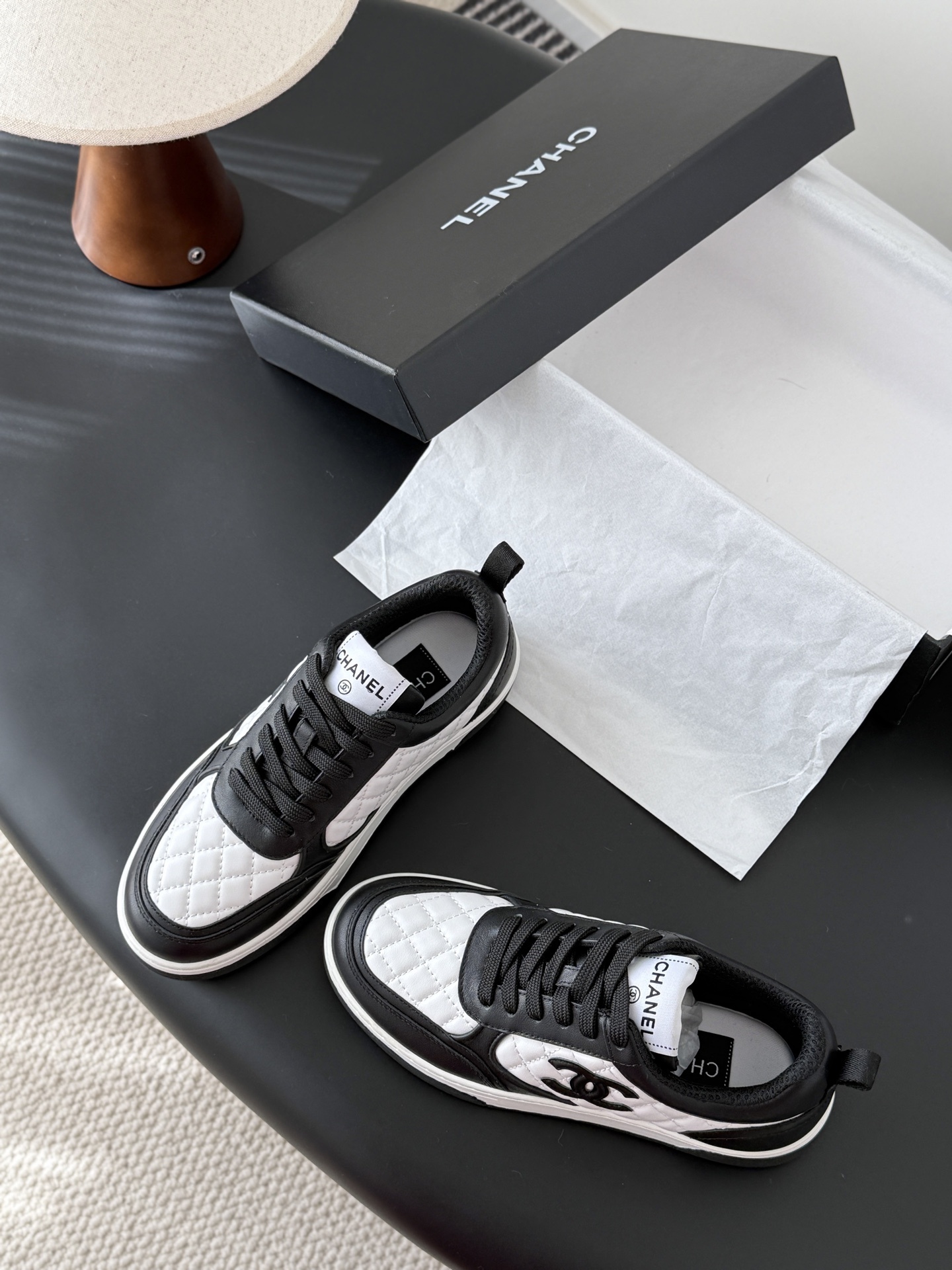 A pair of luxury Chanel black and white quilted leather sneakers with CC logo next to their original black box. - Hình 6