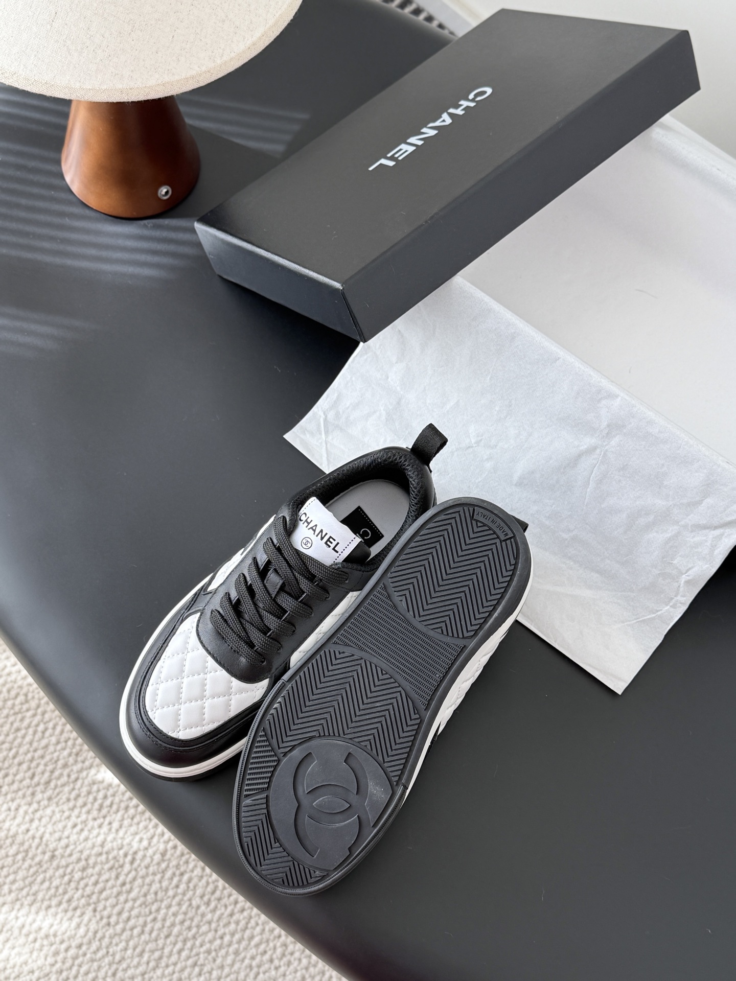 A pair of luxury Chanel black and white quilted leather sneakers with CC logo next to their original black box. - Hình 5