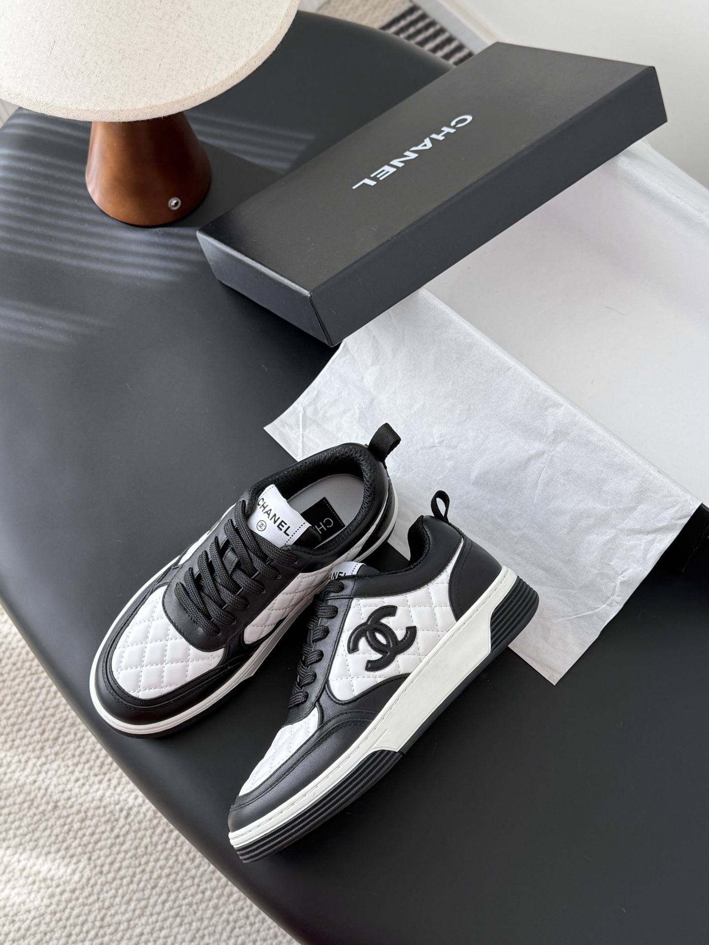A pair of luxury Chanel black and white quilted leather sneakers with CC logo next to their original black box. - Hình 4