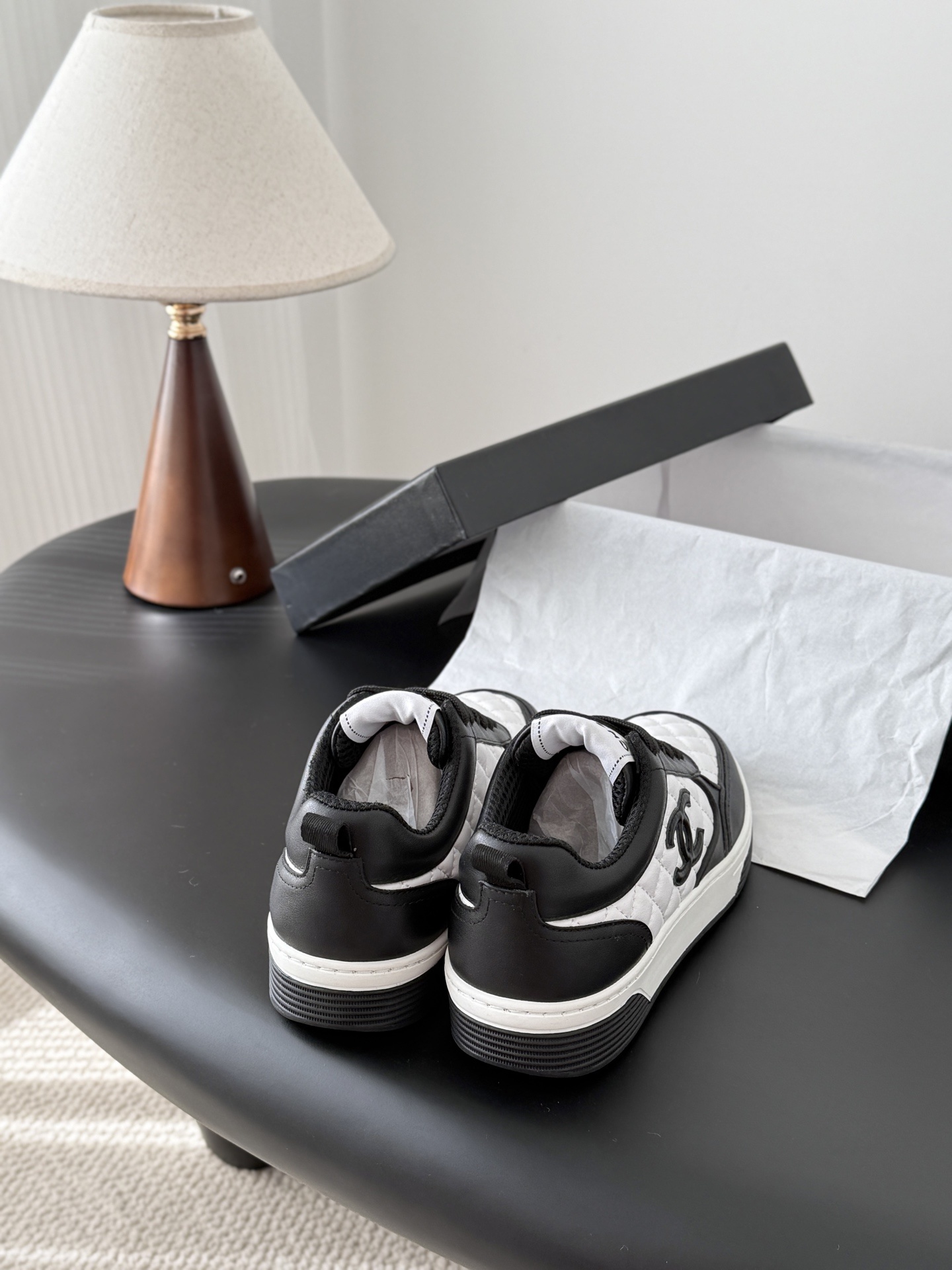 A pair of luxury Chanel black and white quilted leather sneakers with CC logo next to their original black box. - Hình 3