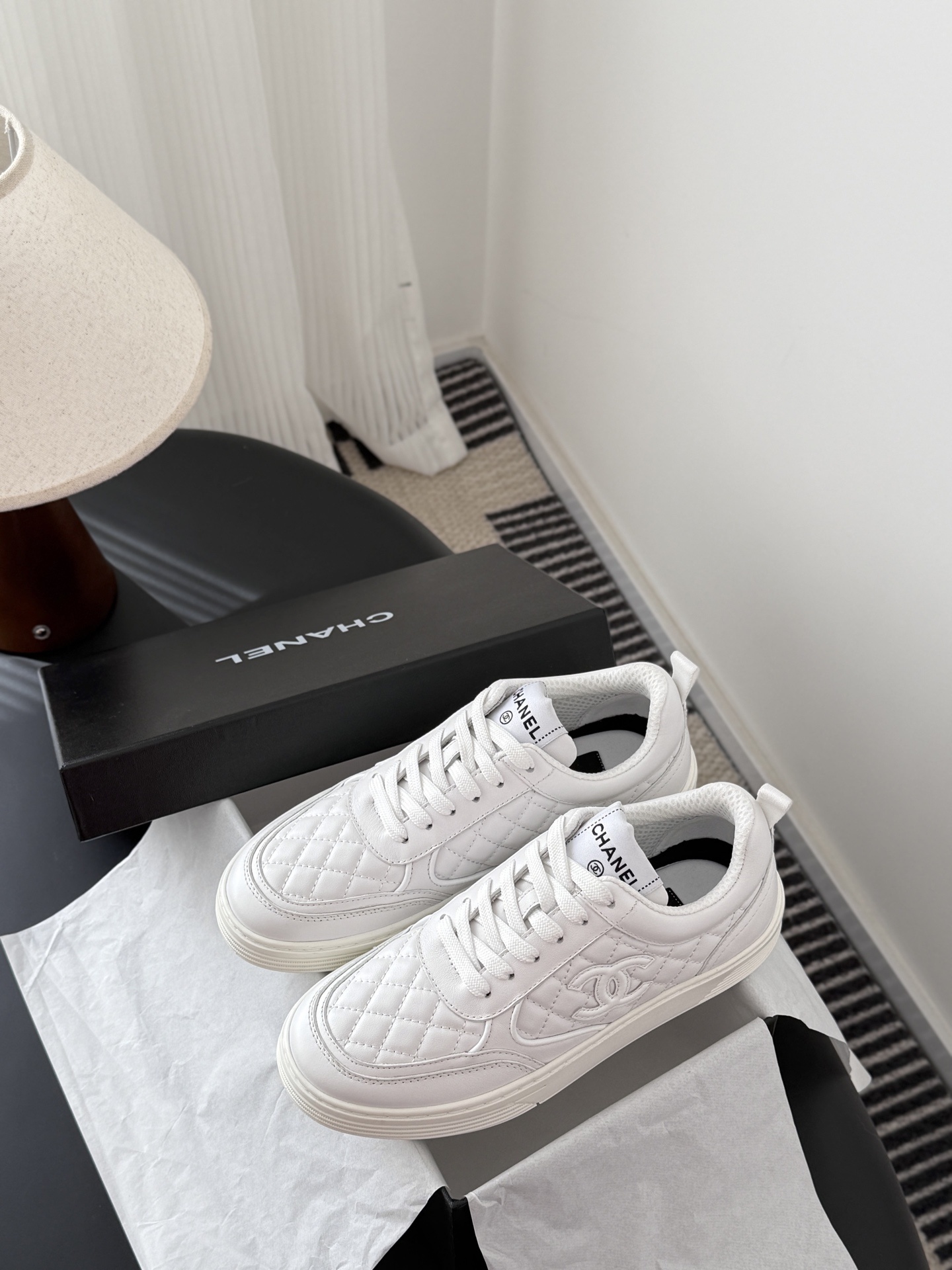 A pair of luxury Chanel white quilted leather sneakers with the CC logo next to their original black box. - Hình 9