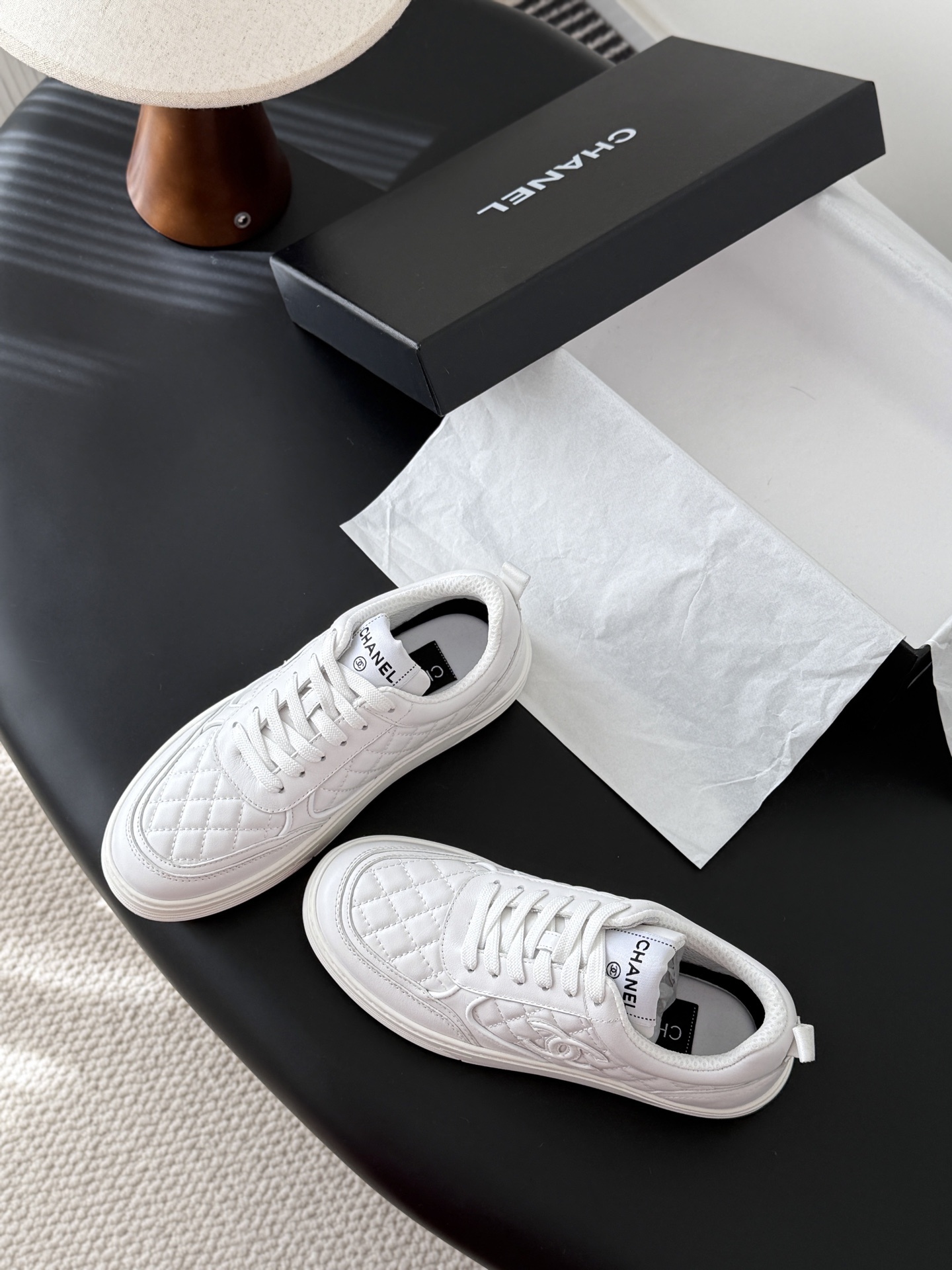 A pair of luxury Chanel white quilted leather sneakers with the CC logo next to their original black box. - Hình 6