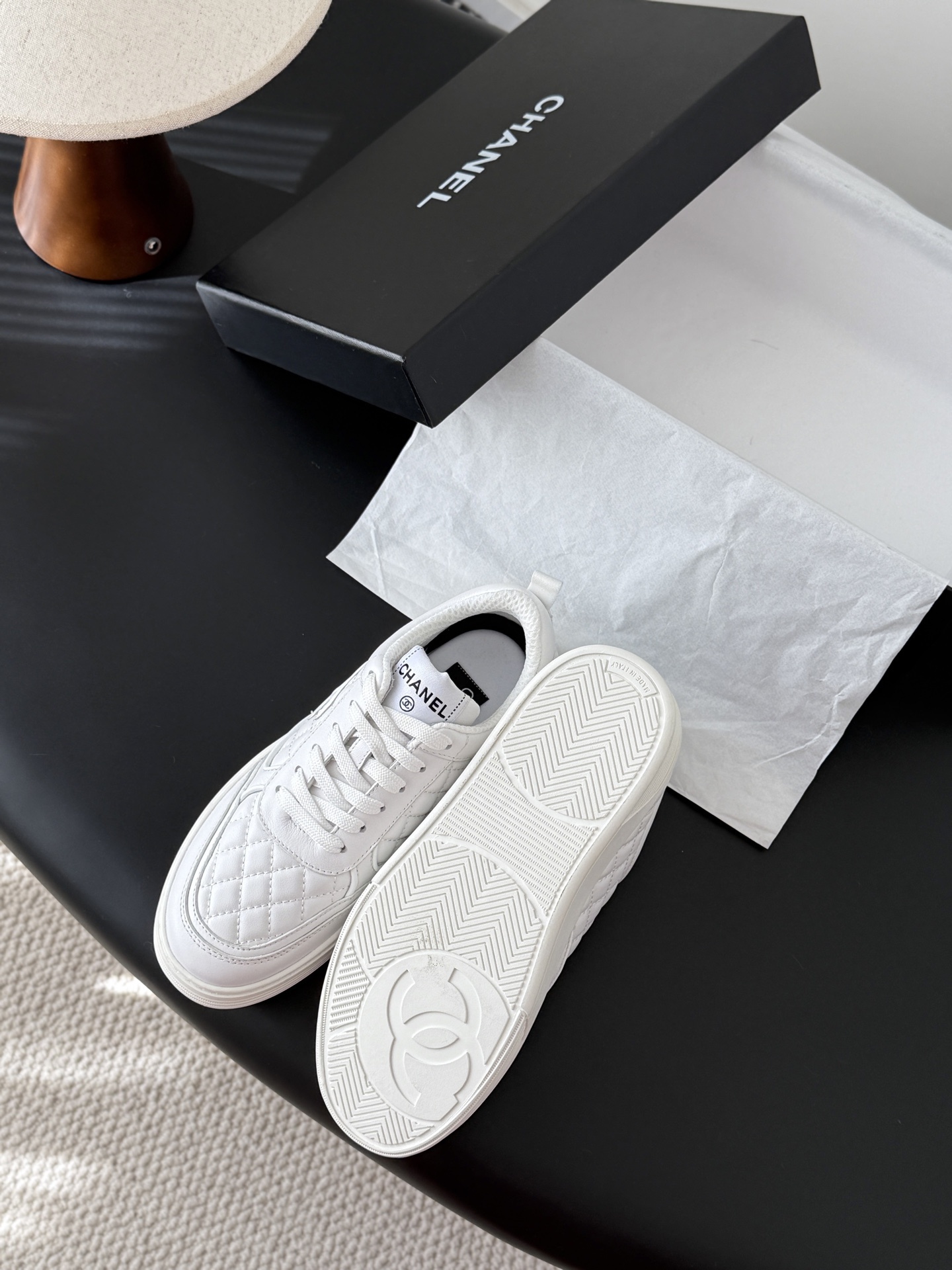 A pair of luxury Chanel white quilted leather sneakers with the CC logo next to their original black box. - Hình 5