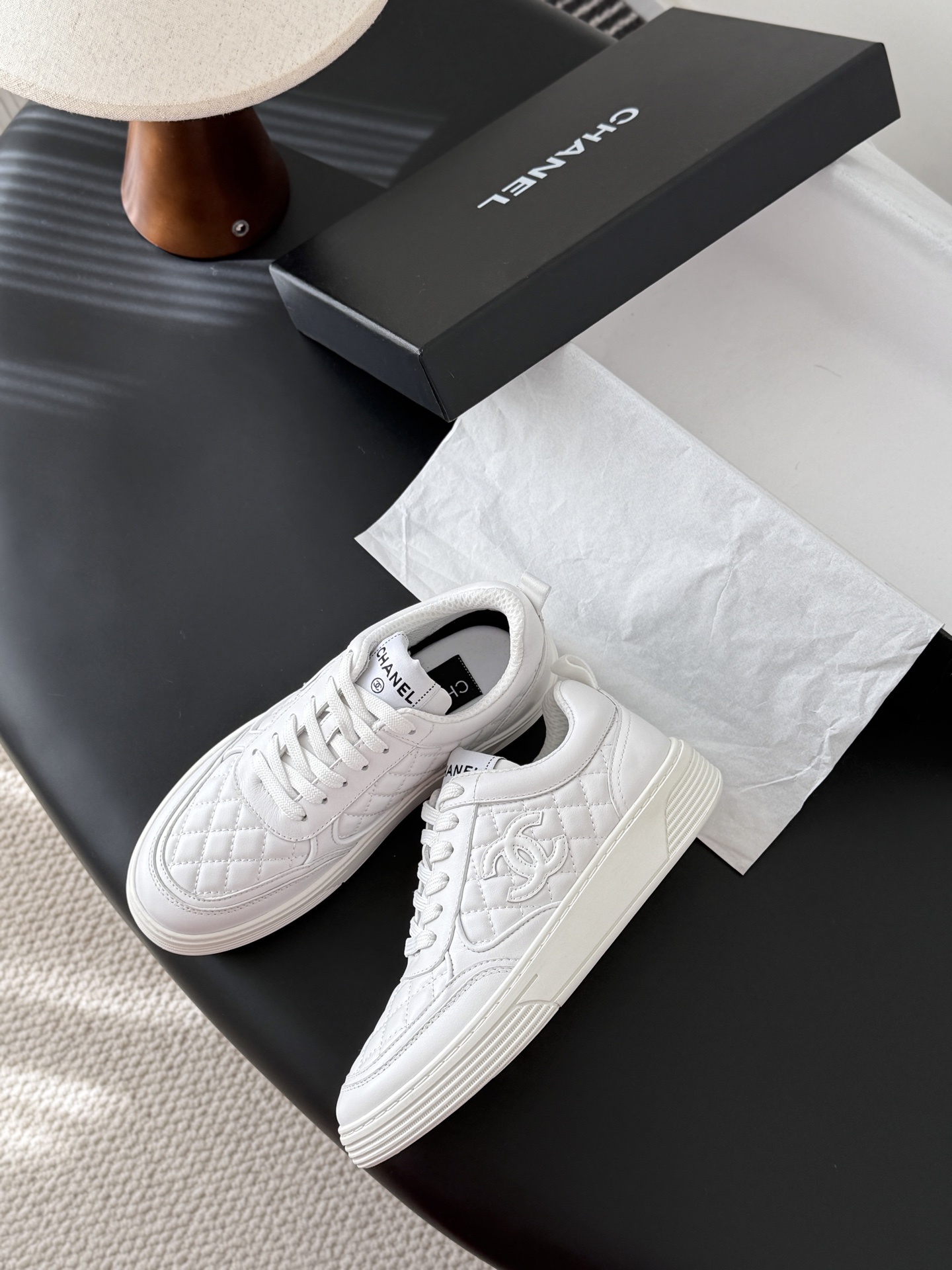 A pair of luxury Chanel white quilted leather sneakers with the CC logo next to their original black box. - Hình 4