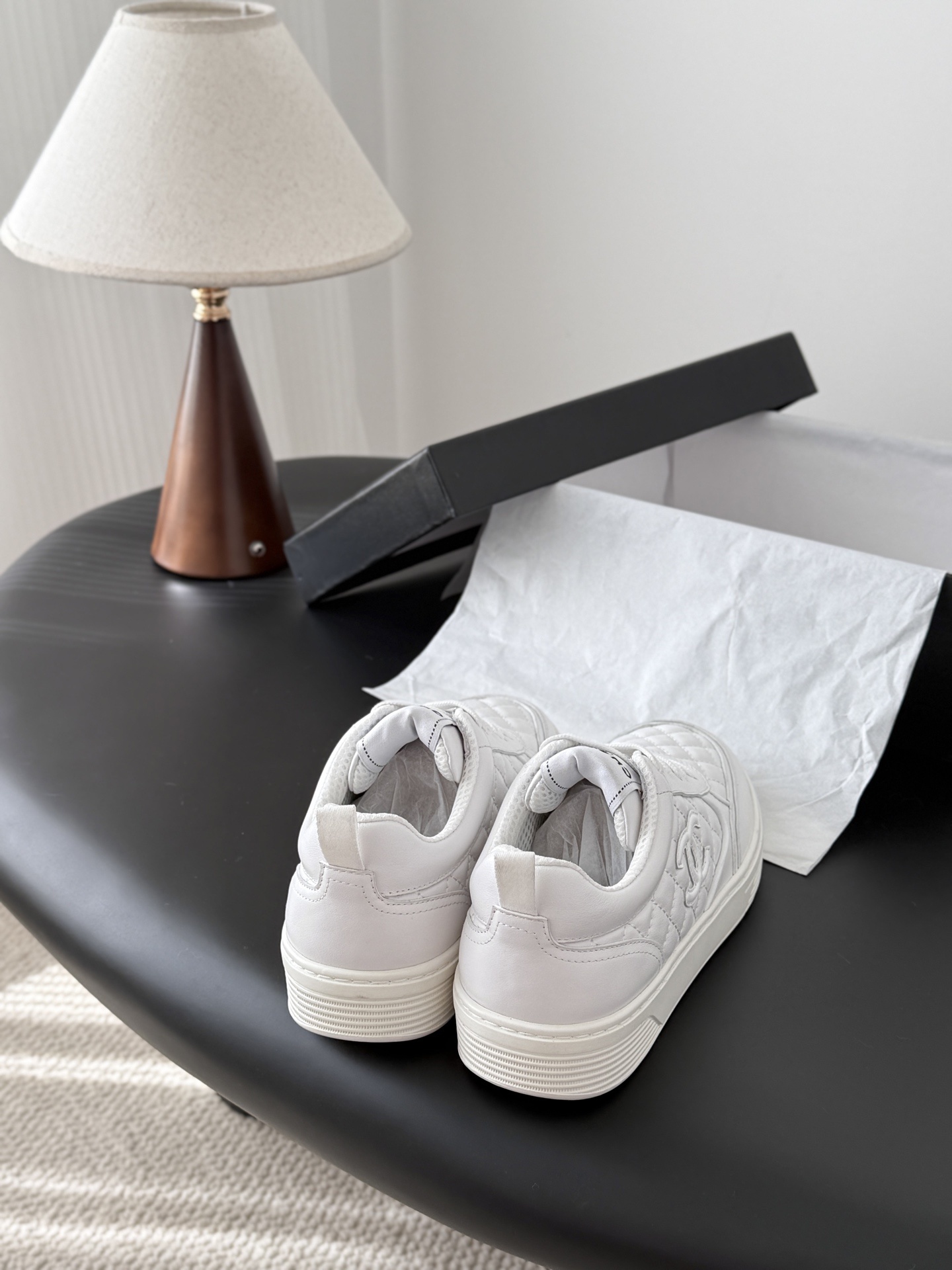 A pair of luxury Chanel white quilted leather sneakers with the CC logo next to their original black box. - Hình 3