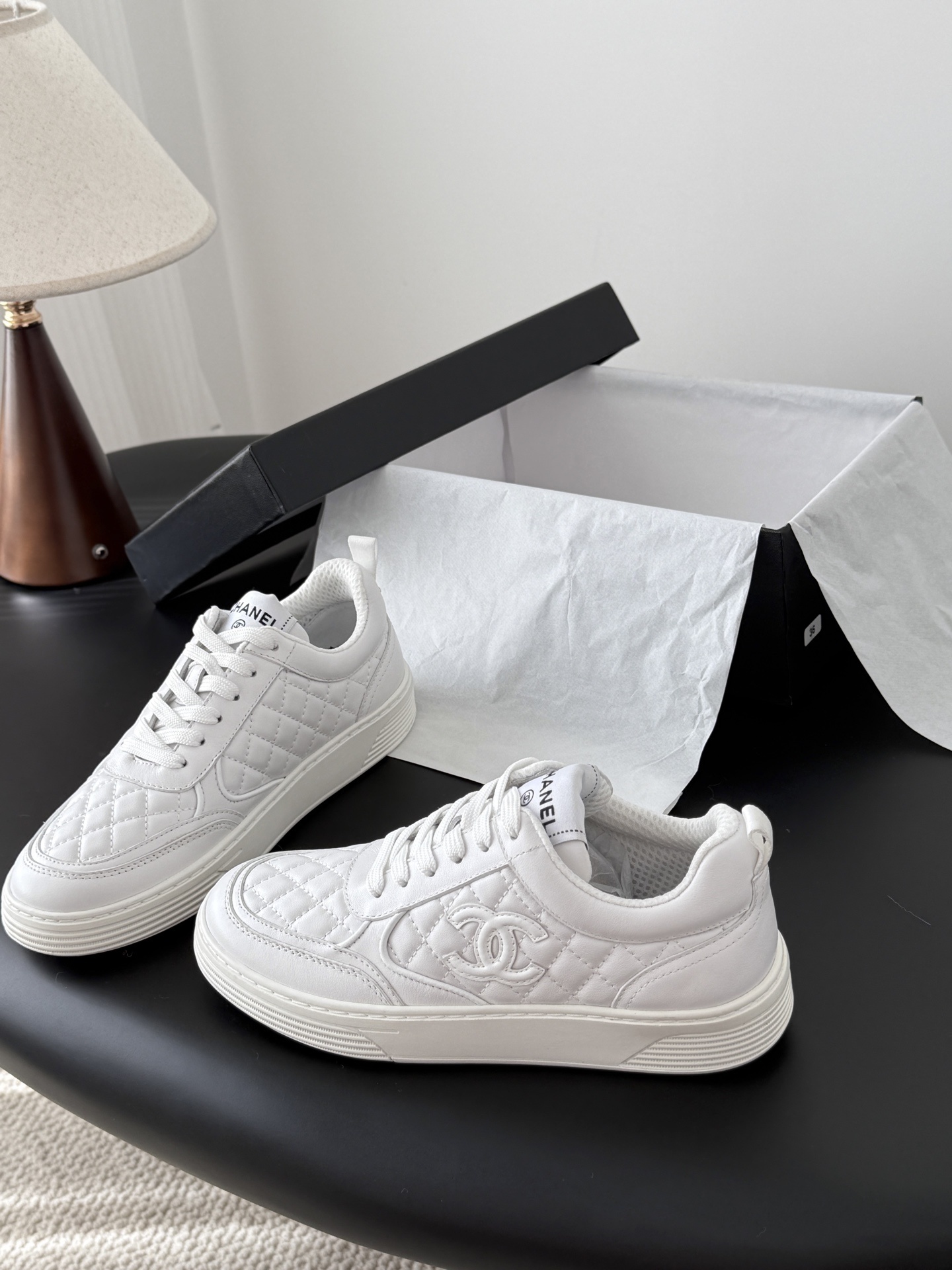 A pair of luxury Chanel white quilted leather sneakers with the CC logo next to their original black box. - Hình 2