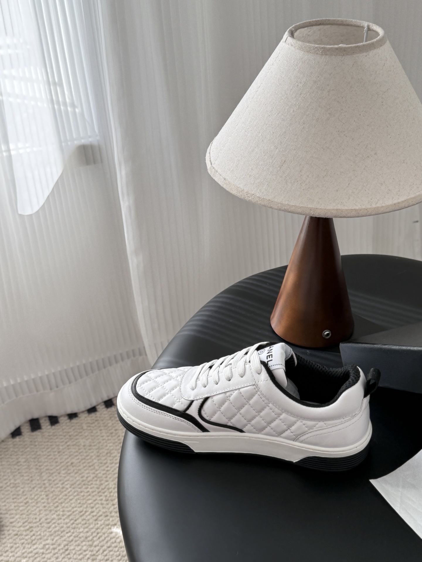 A pair of luxury Chanel white quilted leather sneakers with black CC logo and black designer shoebox on a table. - Hình 8