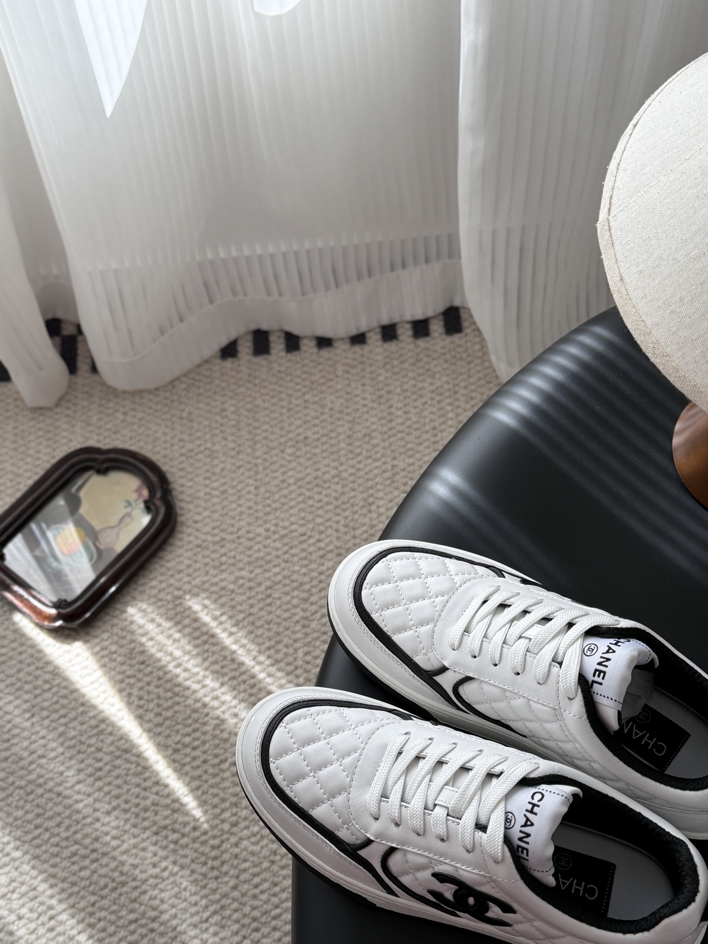 A pair of luxury Chanel white quilted leather sneakers with black CC logo and black designer shoebox on a table. - Hình 7