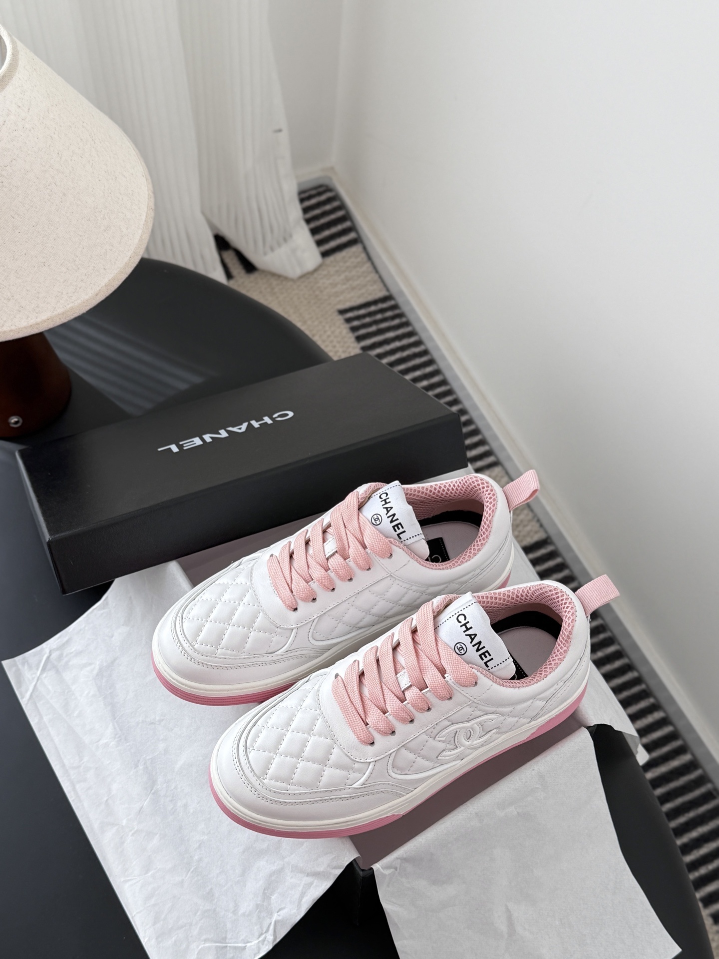 Pair of Chanel white quilted leather sneakers with pink laces and pink soles next to a black Chanel box - Hình 9