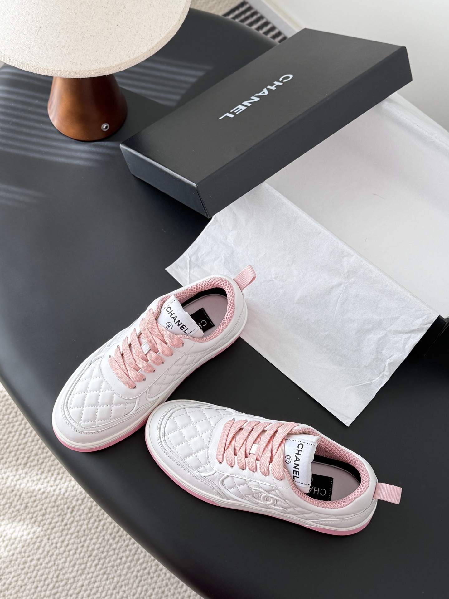 Pair of Chanel white quilted leather sneakers with pink laces and pink soles next to a black Chanel box - Hình 6
