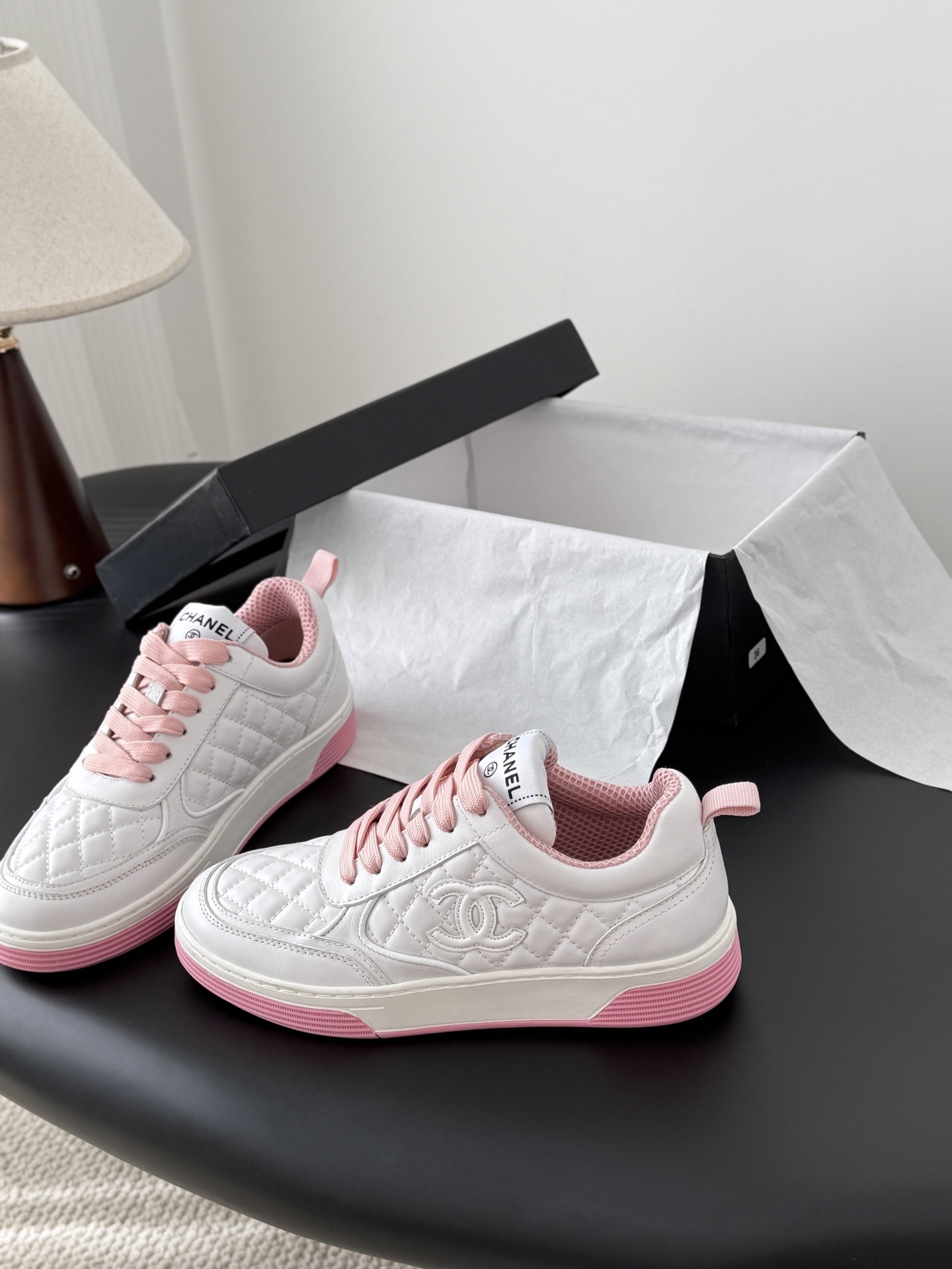 Pair of Chanel white quilted leather sneakers with pink laces and pink soles next to a black Chanel box - Hình 2
