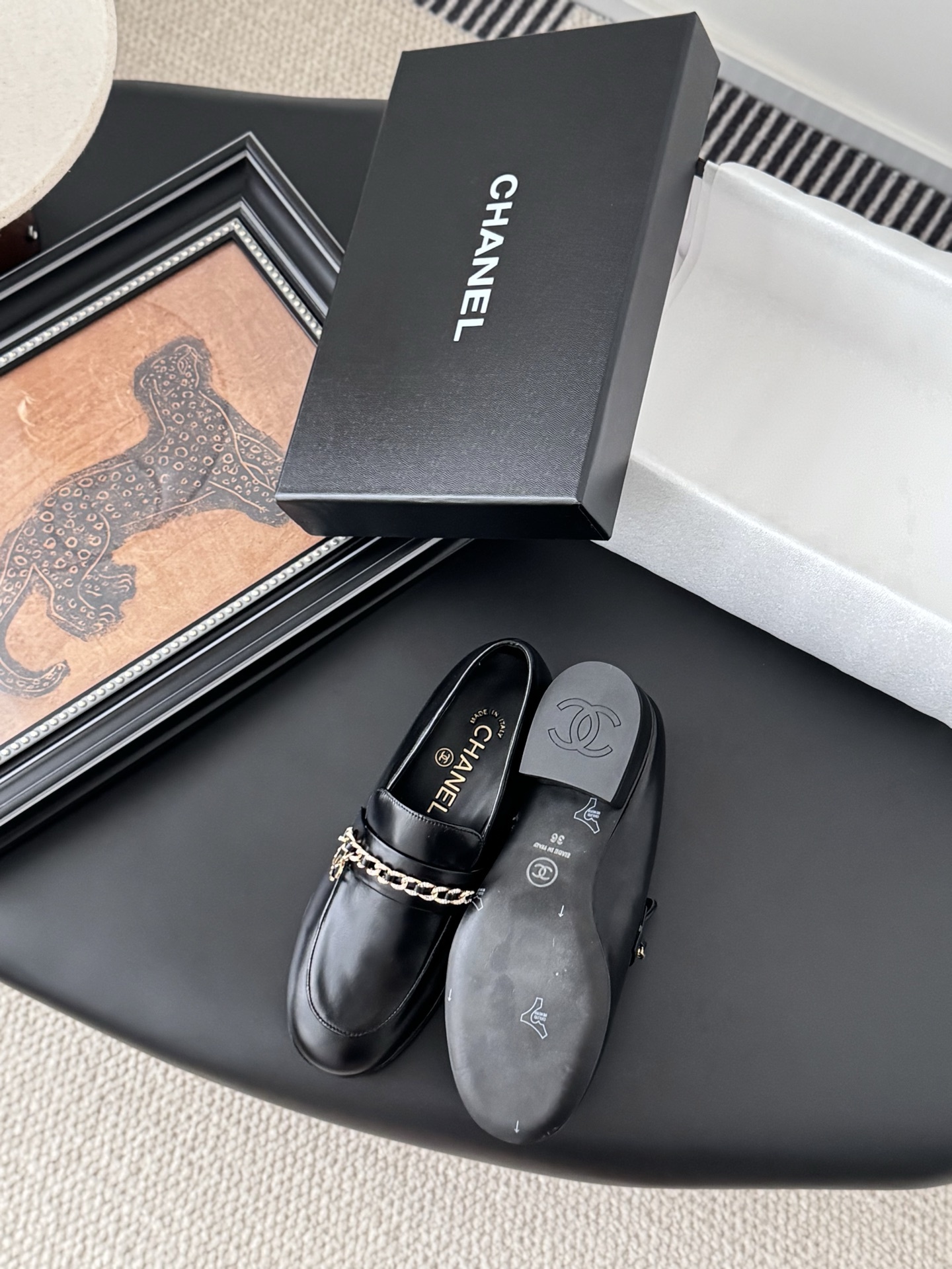 Pair of black Chanel leather loafers with gold chain and CC logo detail next to original box - Hình 4
