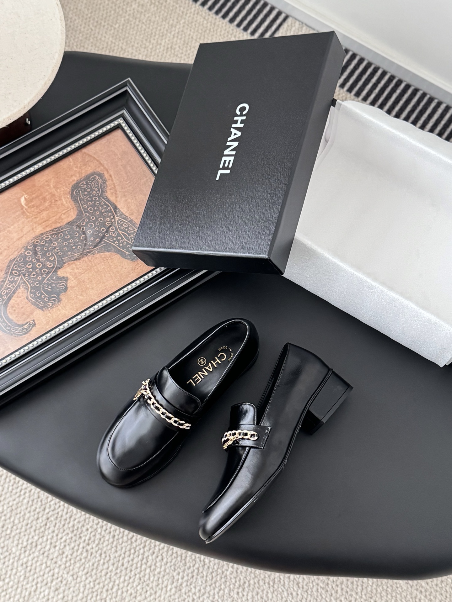 Pair of black Chanel leather loafers with gold chain and CC logo detail next to original box - Hình 3