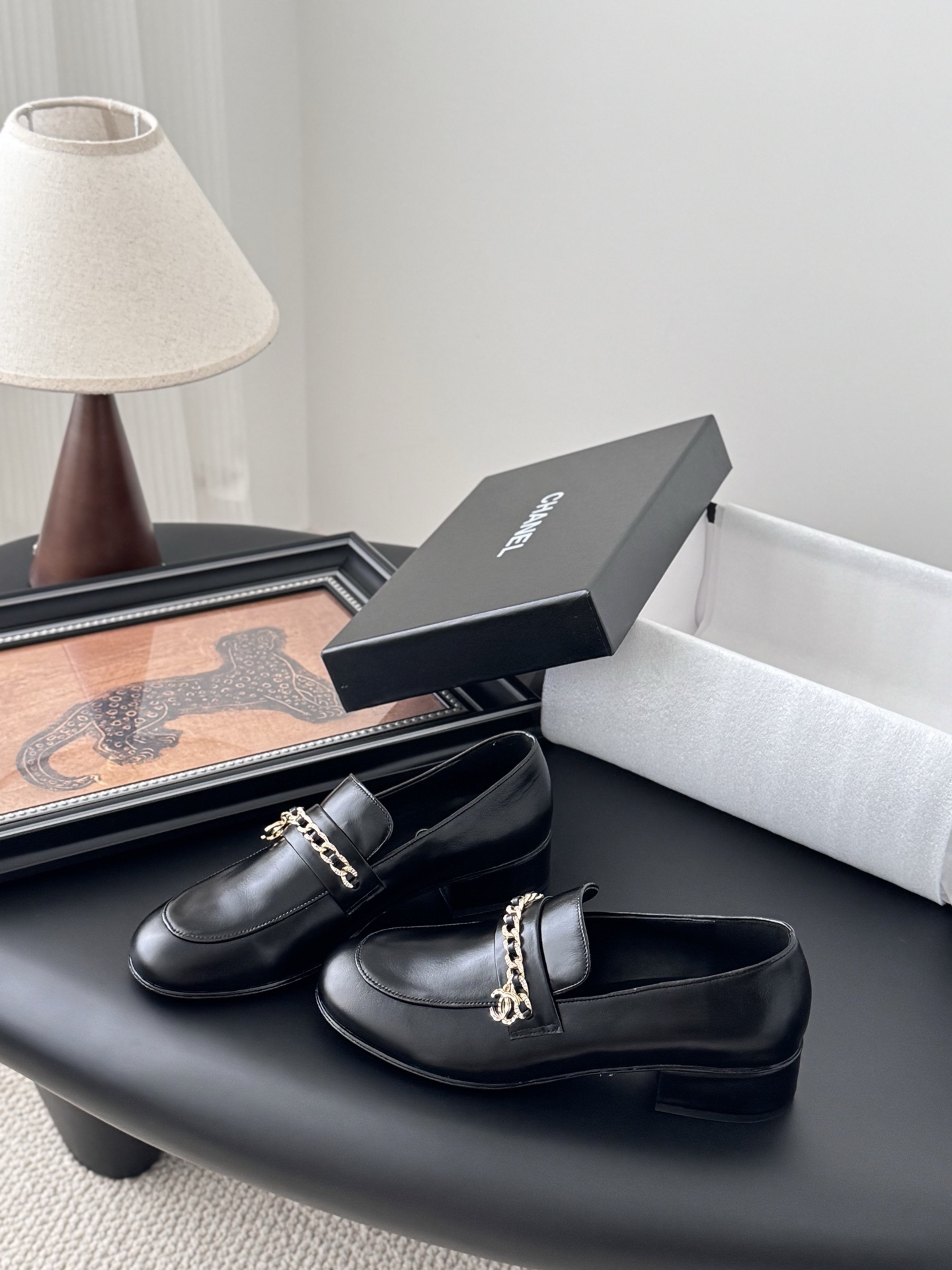 Pair of black Chanel leather loafers with gold chain and CC logo detail next to original box - Hình 2