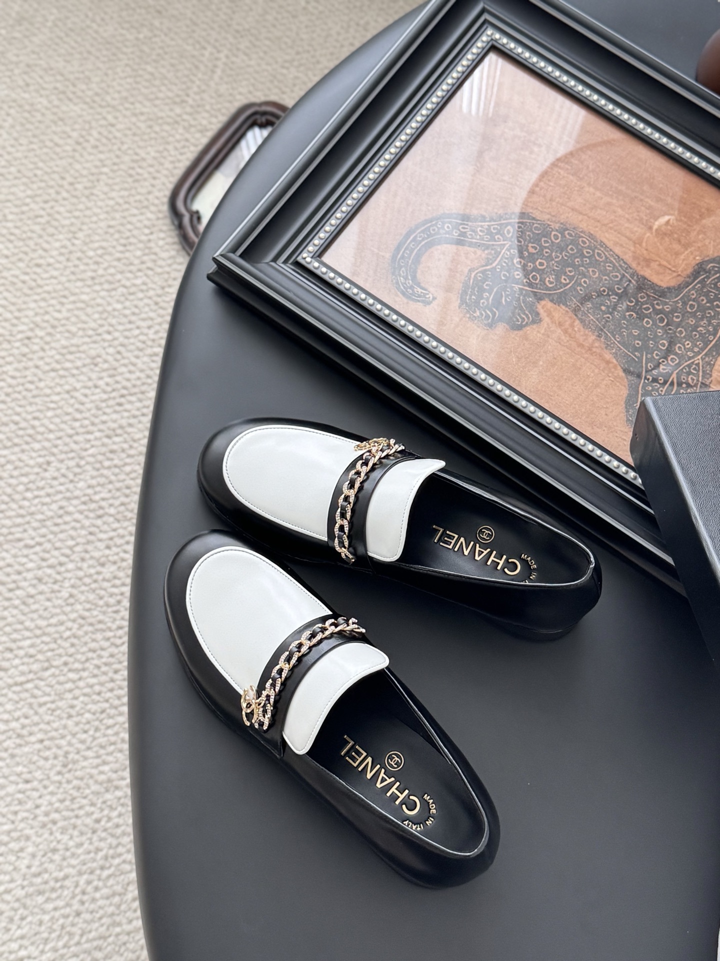 A pair of Chanel black and white leather loafers with gold-tone chain and CC logo sitting next to a Chanel shoe box. - Hình 5